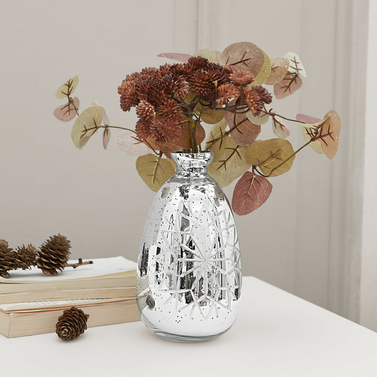 Vase Zorelie Vase en verre argenté avec motif gravé et fleurs séchées brunes sur une table blanche
