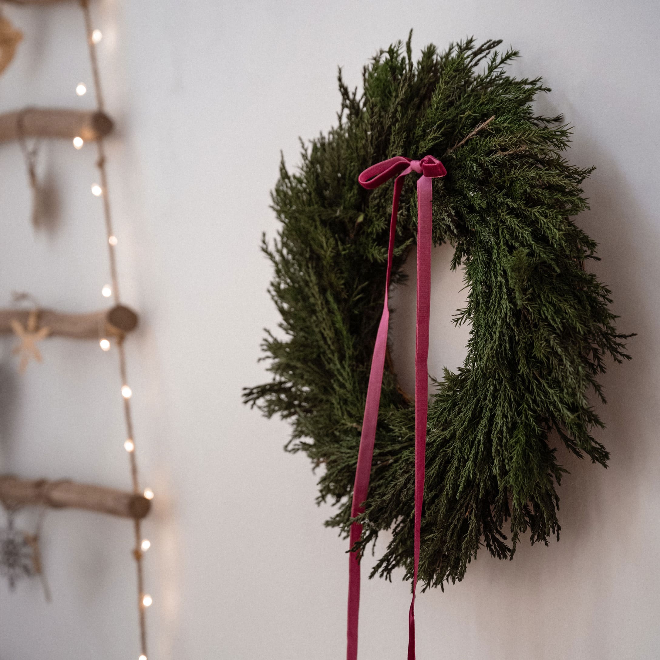 Couronne de Noël verte avec ruban en velours rouge accrochée à un mur blanc, décoration festive
