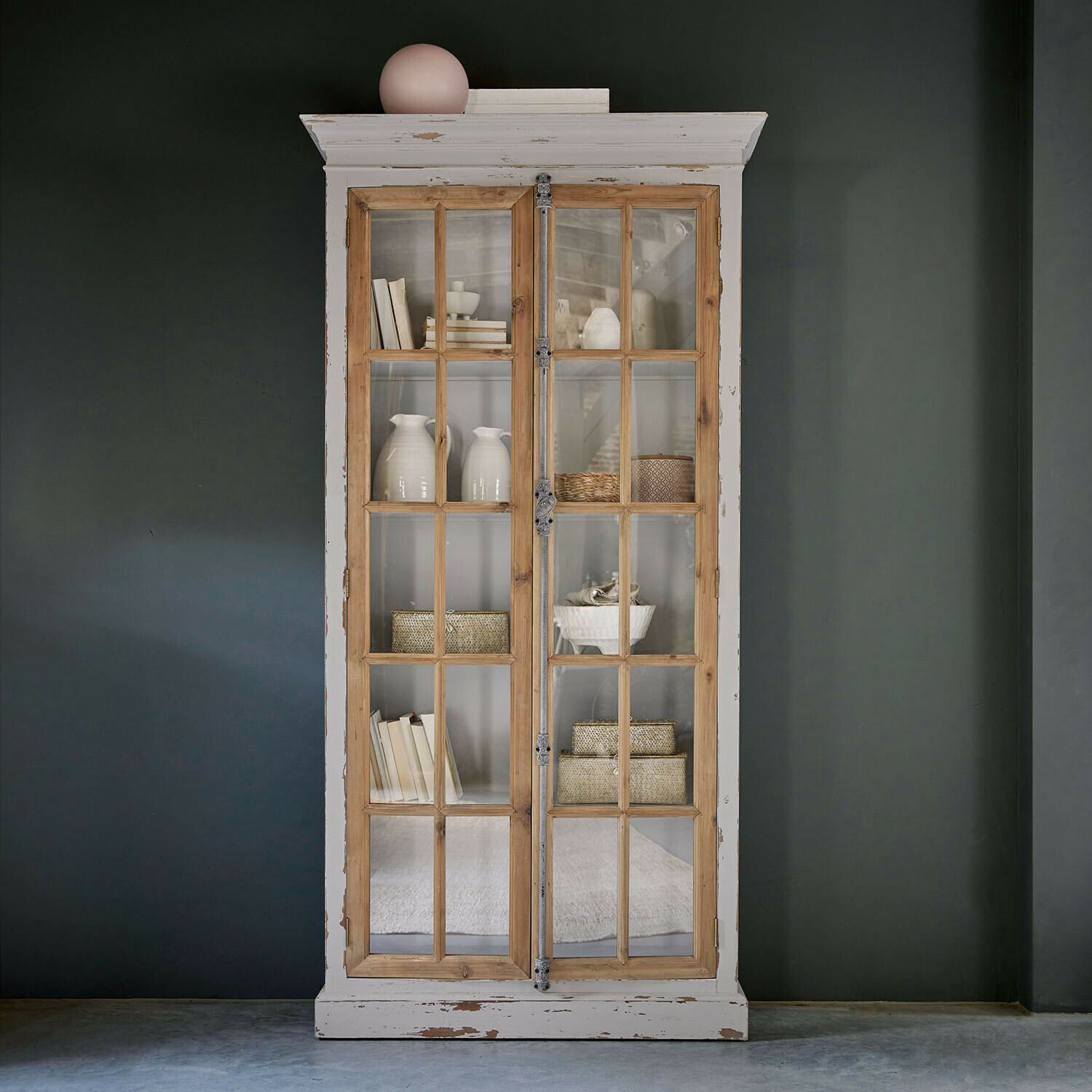 Vitrine Philippe Vitrine en bois avec cadre blanc vieilli et portes vitrées, décorations et livres à l'intérieur