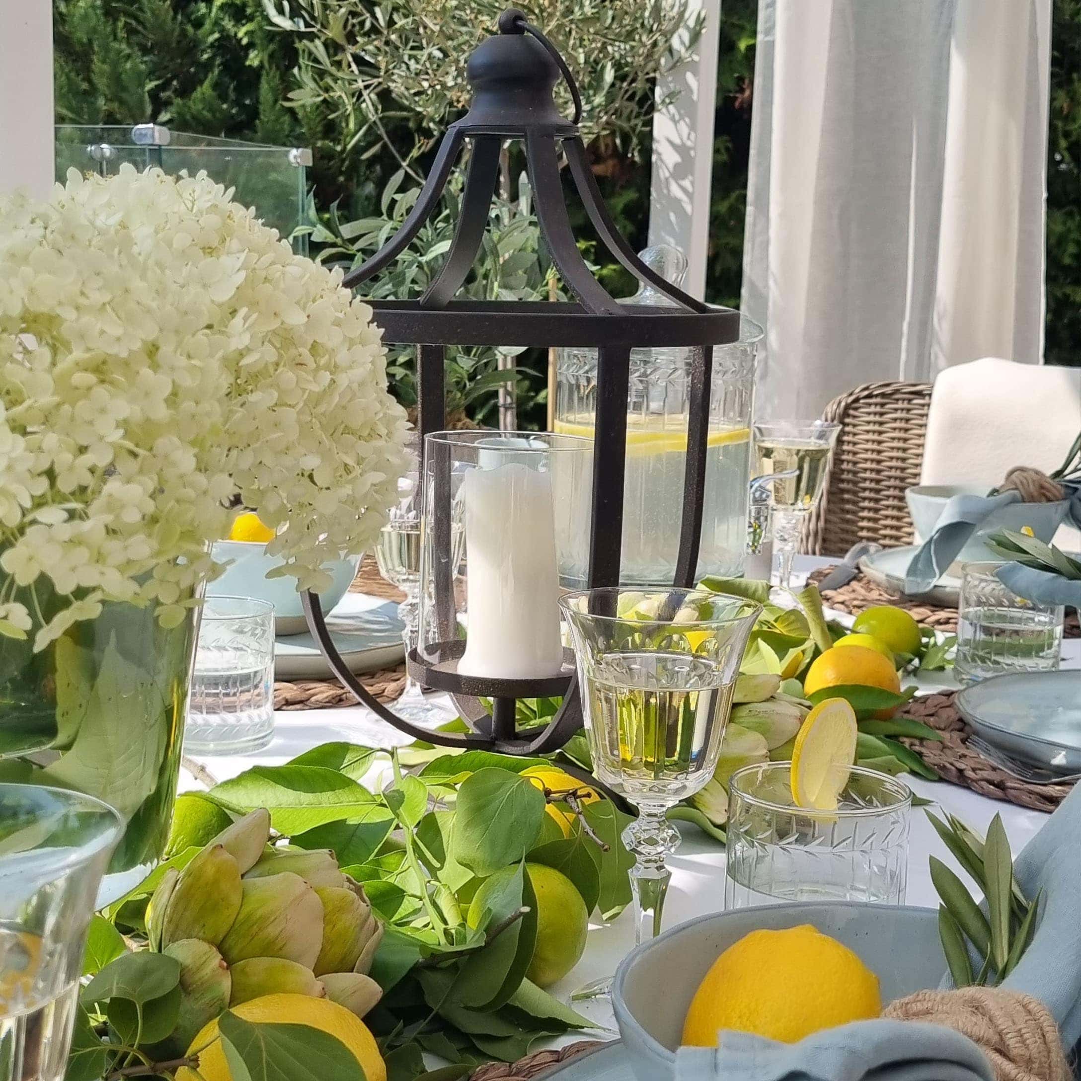 Lanterne en métal noir avec bougie blanche sur une table d'été décorée de citrons et de feuillage vert