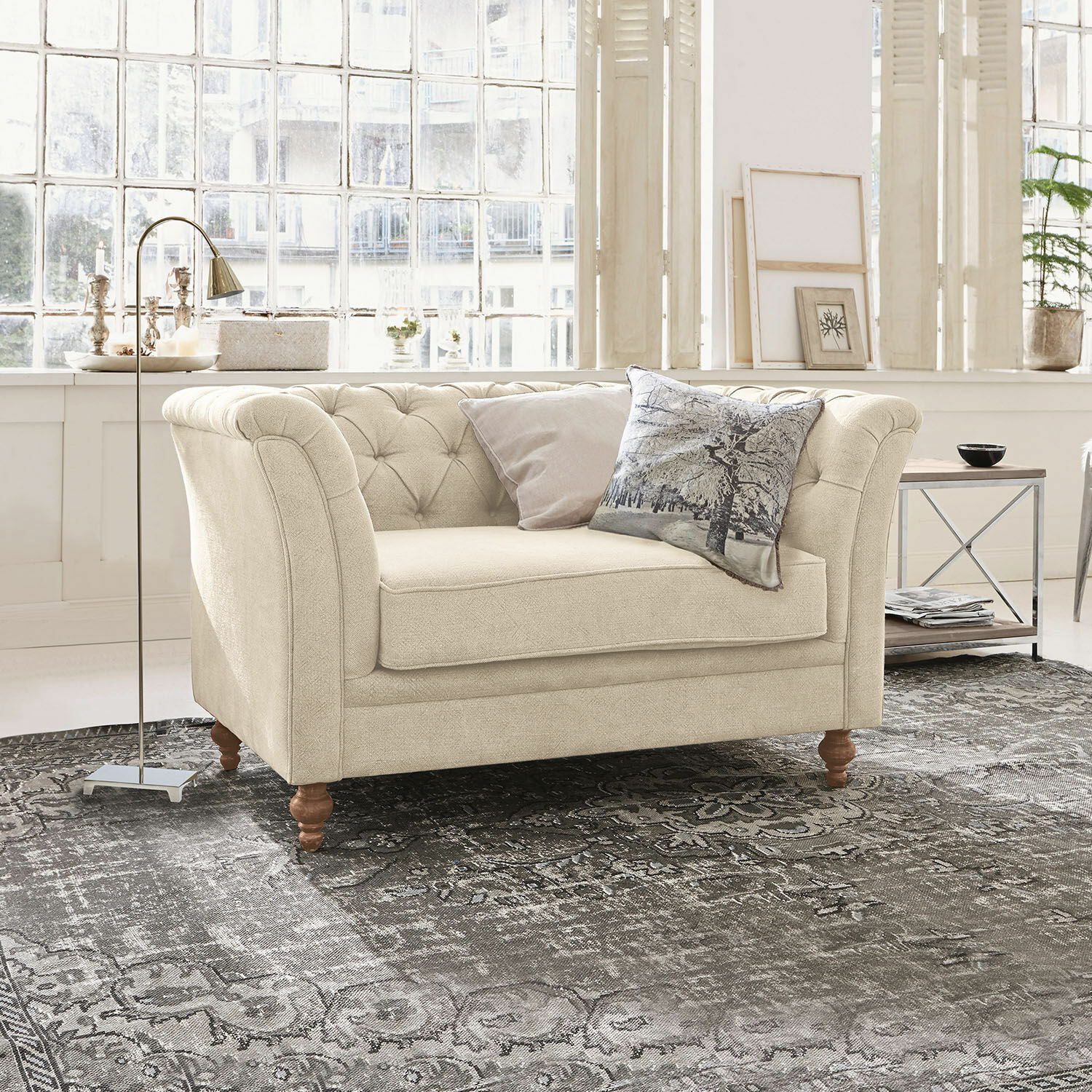Canapé Clères Canapé beige en tissu avec dossier capitonné et pieds en bois sur un tapis gris dans un salon lumineux