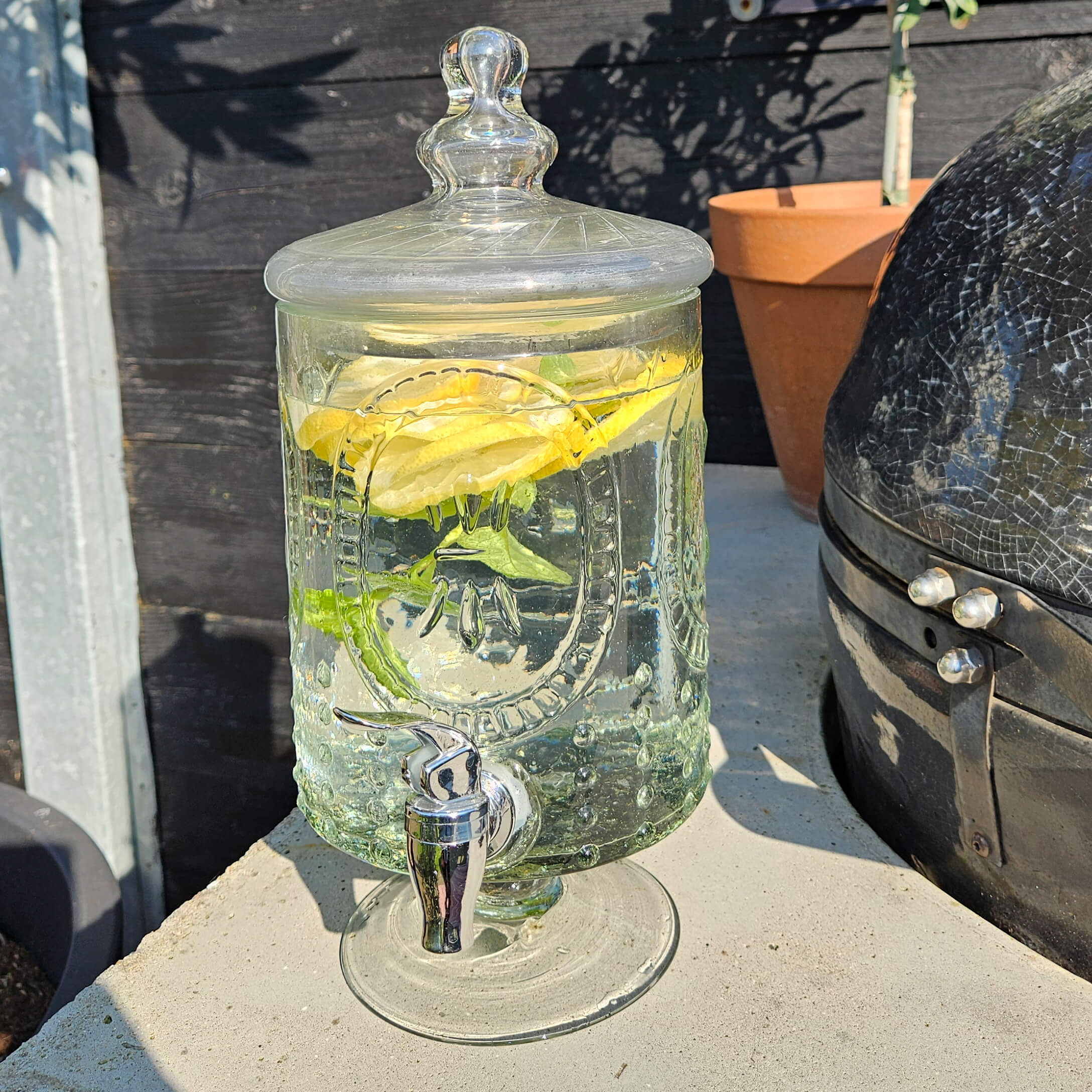 Distributeur de boisson en verre avec couvercle, rempli d'eau citronnée et menthe, parfait pour l'été