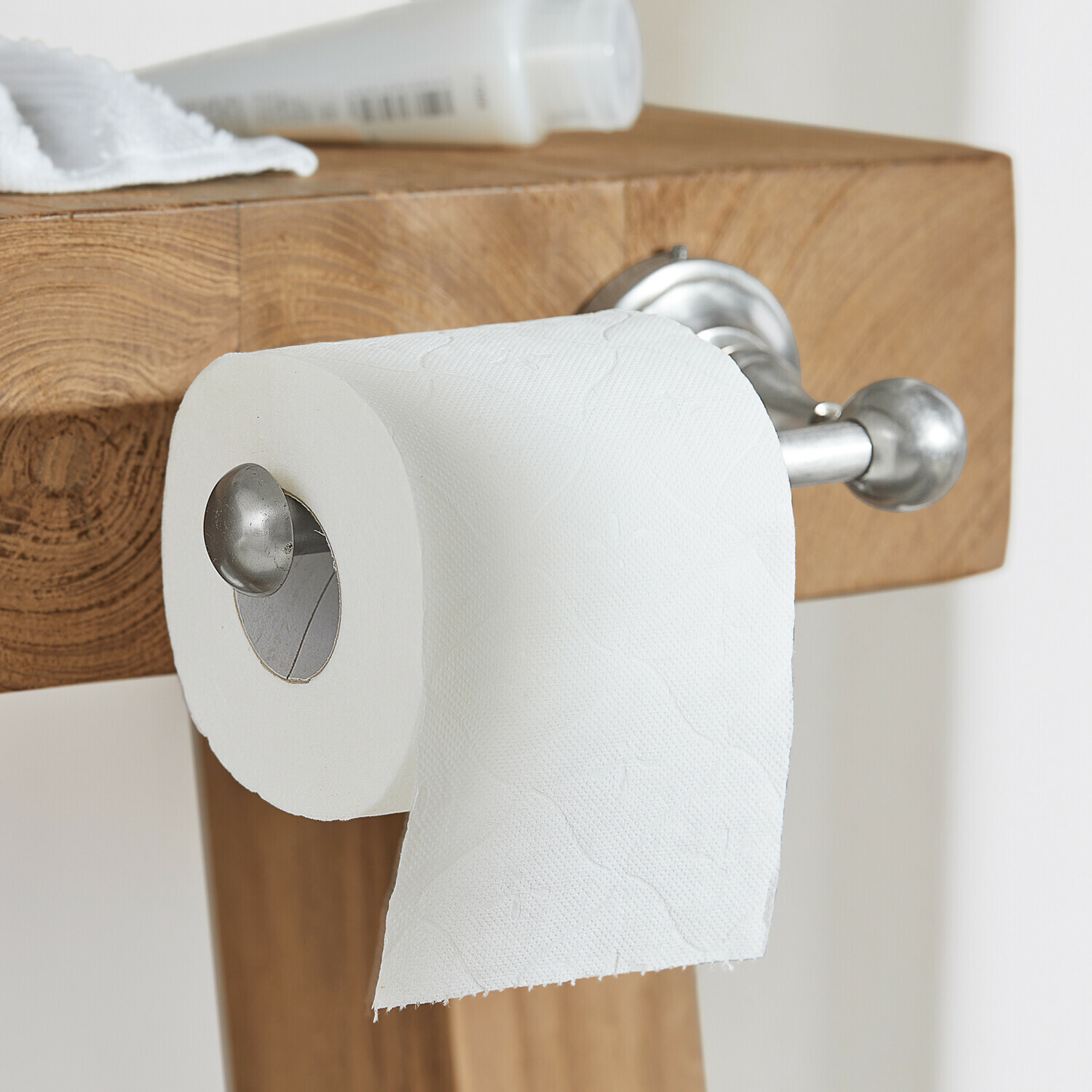Porte-papier toilette Pax Porte-papier toilette en acier inoxydable fixé sur un plan de travail en bois dans une salle de bain