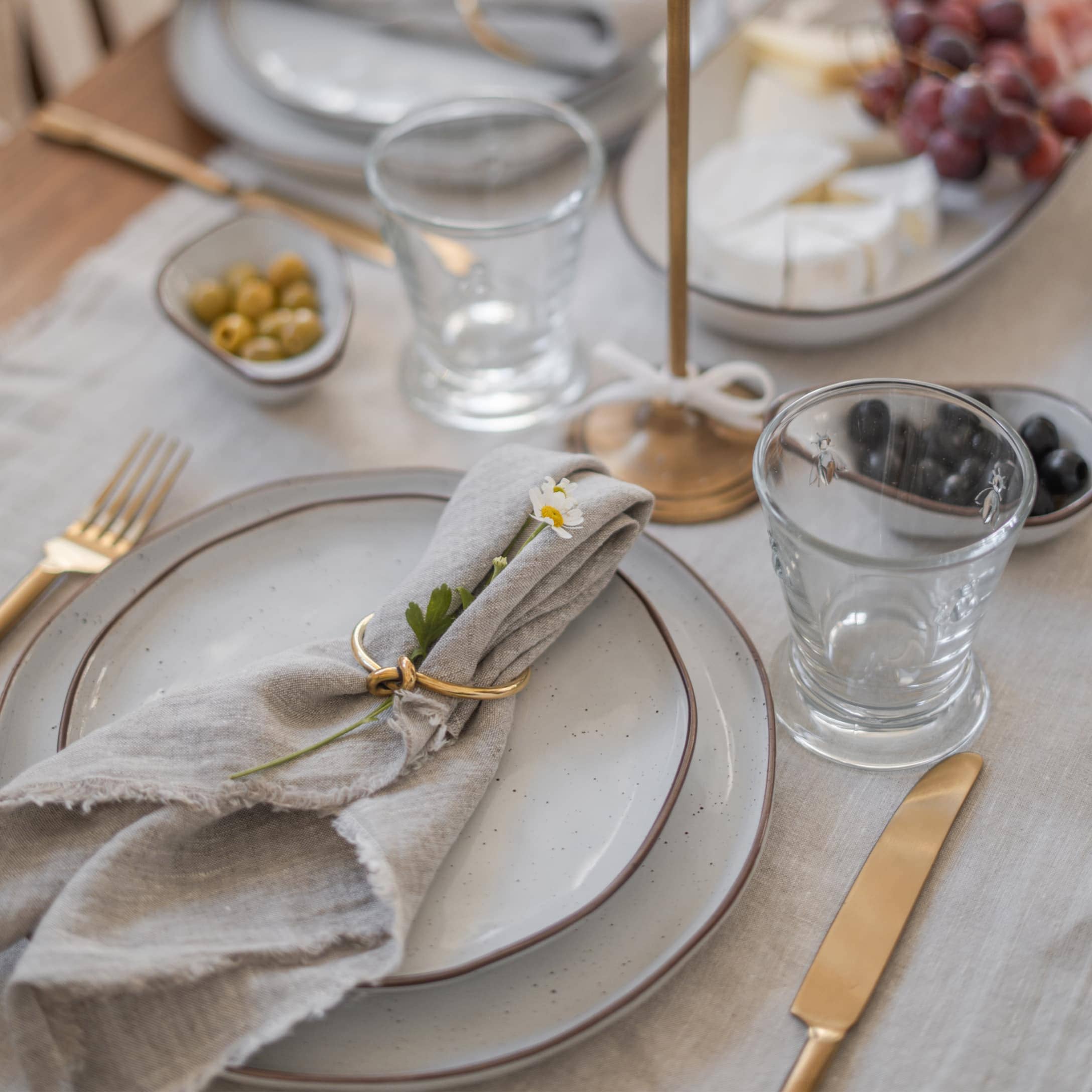 Service de table élégant avec assiettes grises, couverts dorés et serviette en lin ornée d'une fleur