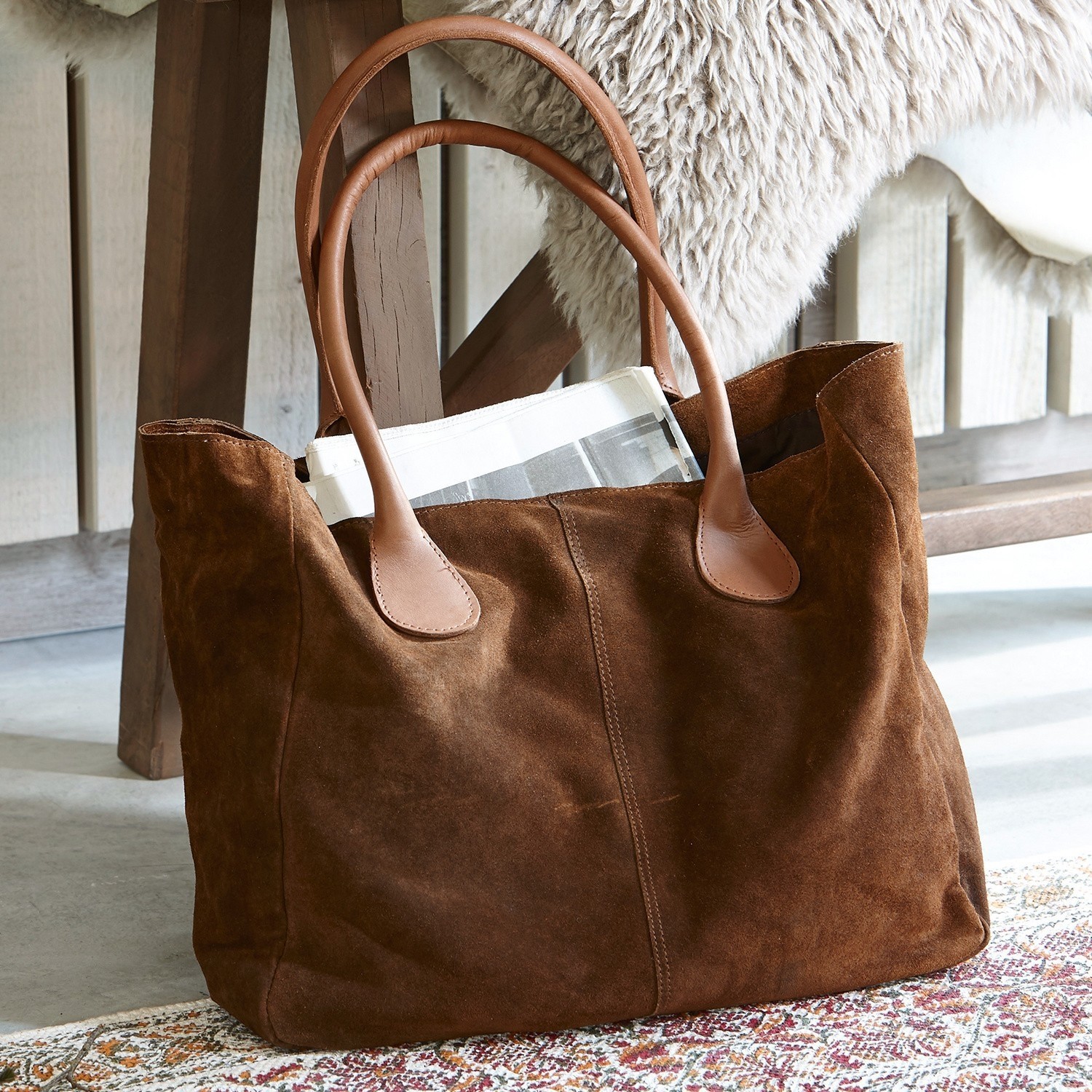 Sac Genevielle Sac en daim marron avec poignées en cuir clair posé sur un tapis coloré près d'une chaise en bois