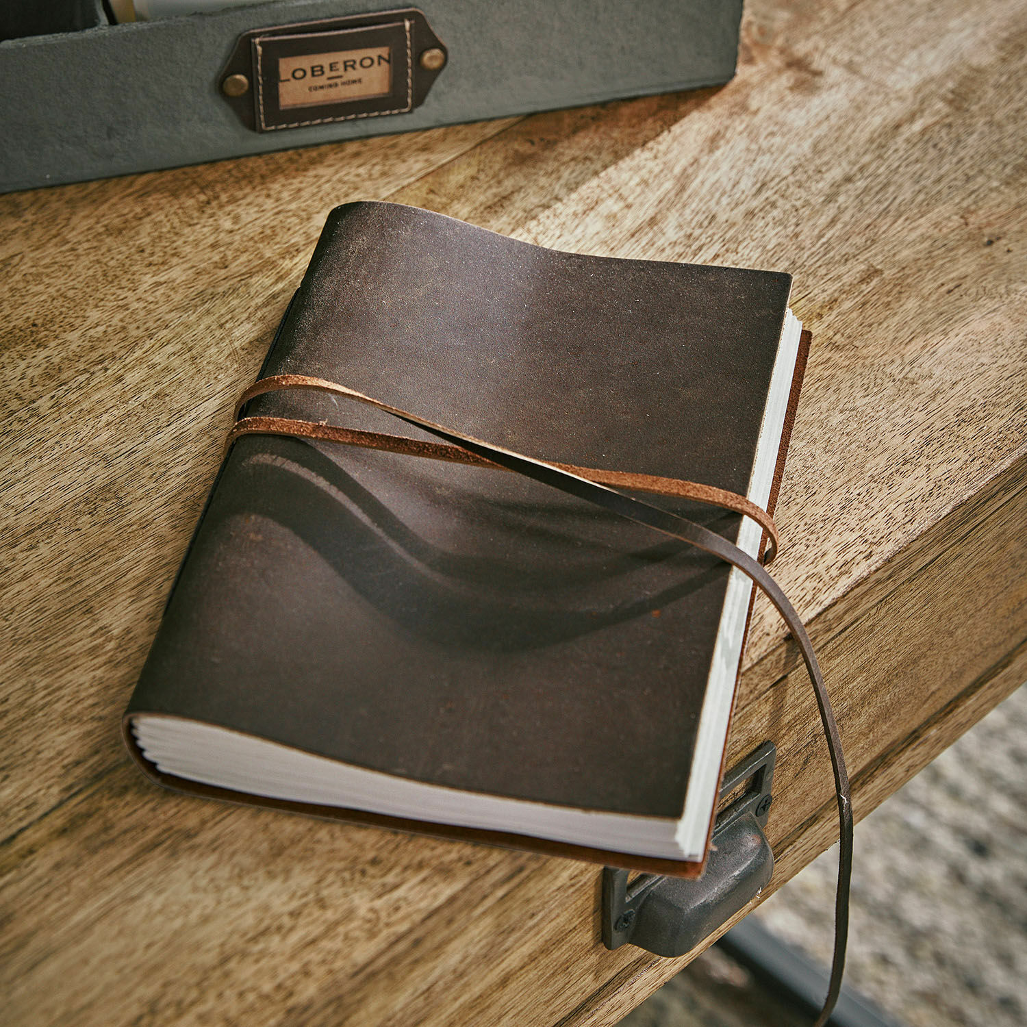 Carnet Rédené Carnet en cuir marron avec lanière posé sur un bureau en bois, accessoire d'écriture pratique