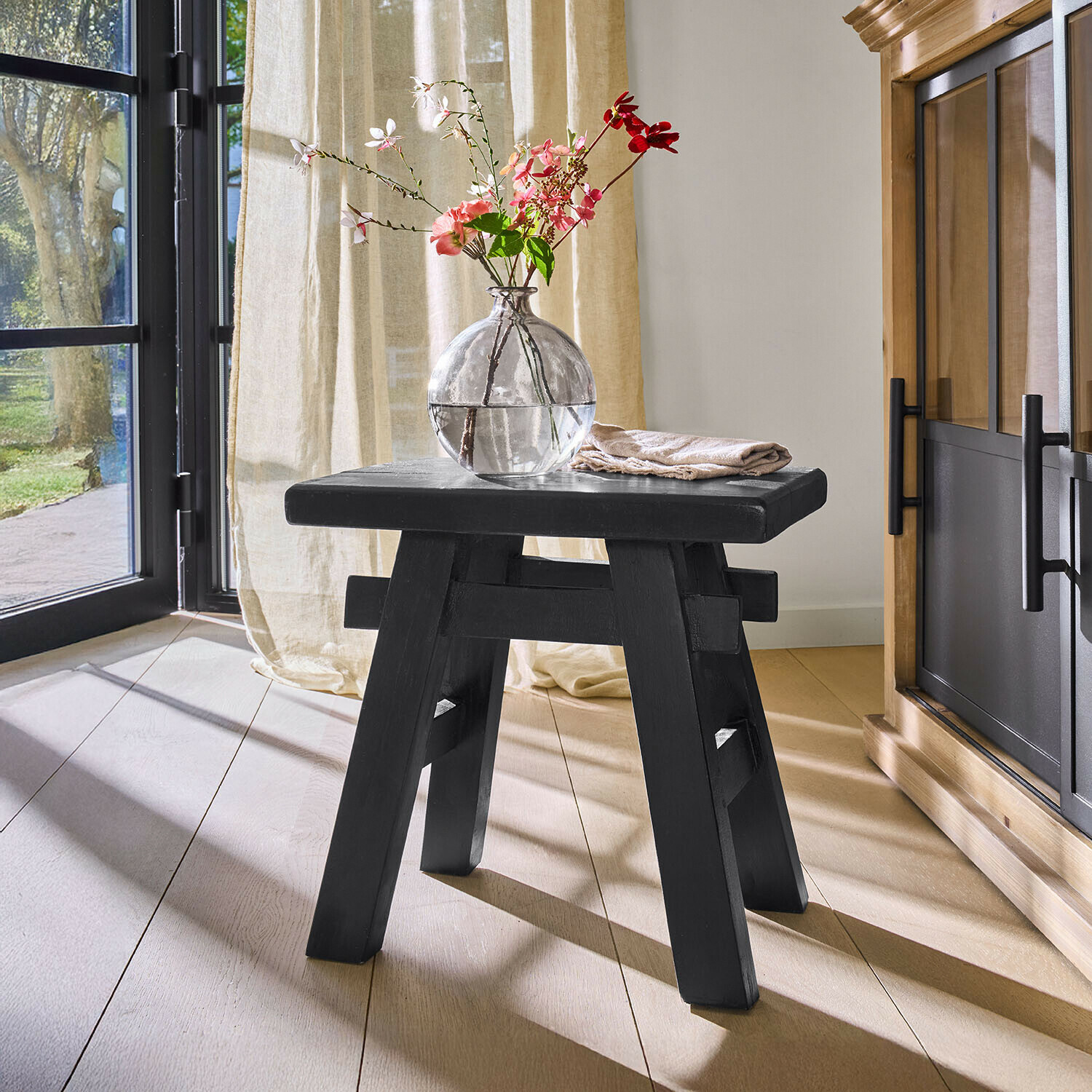 Tabouret Oaklynne Tabouret en bois noir au design simple dans une pièce lumineuse avec vase et fleurs