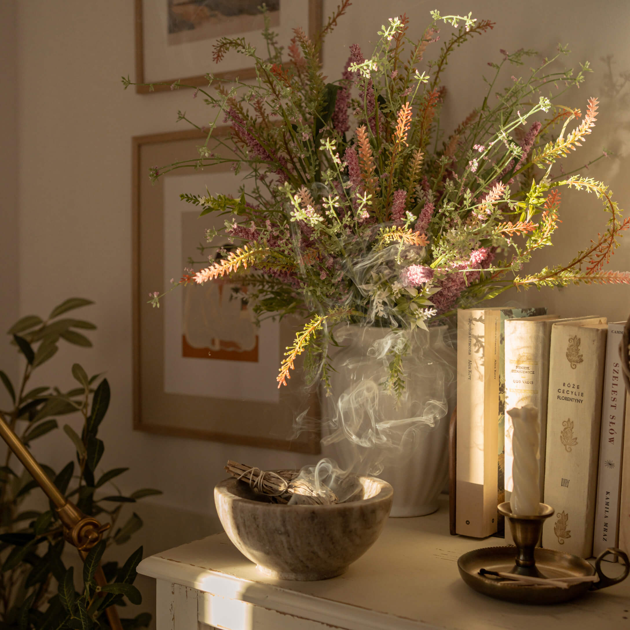 Bol en albâtre avec sauge fumante à côté d'un vase de fleurs colorées et de livres sur une table