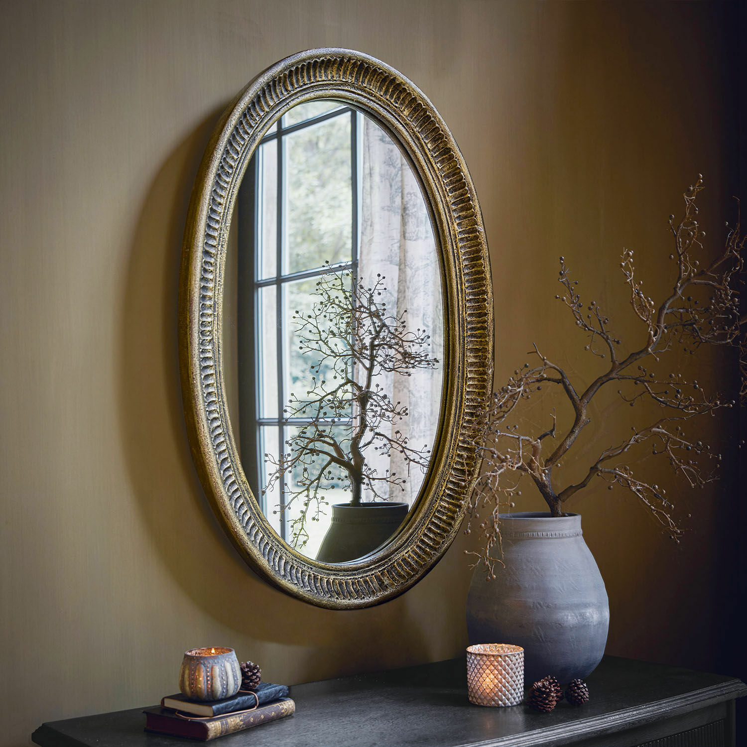 Miroir Boissiére Miroir ovale avec cadre doré vieilli suspendu au mur, décor de table avec vase et bougies