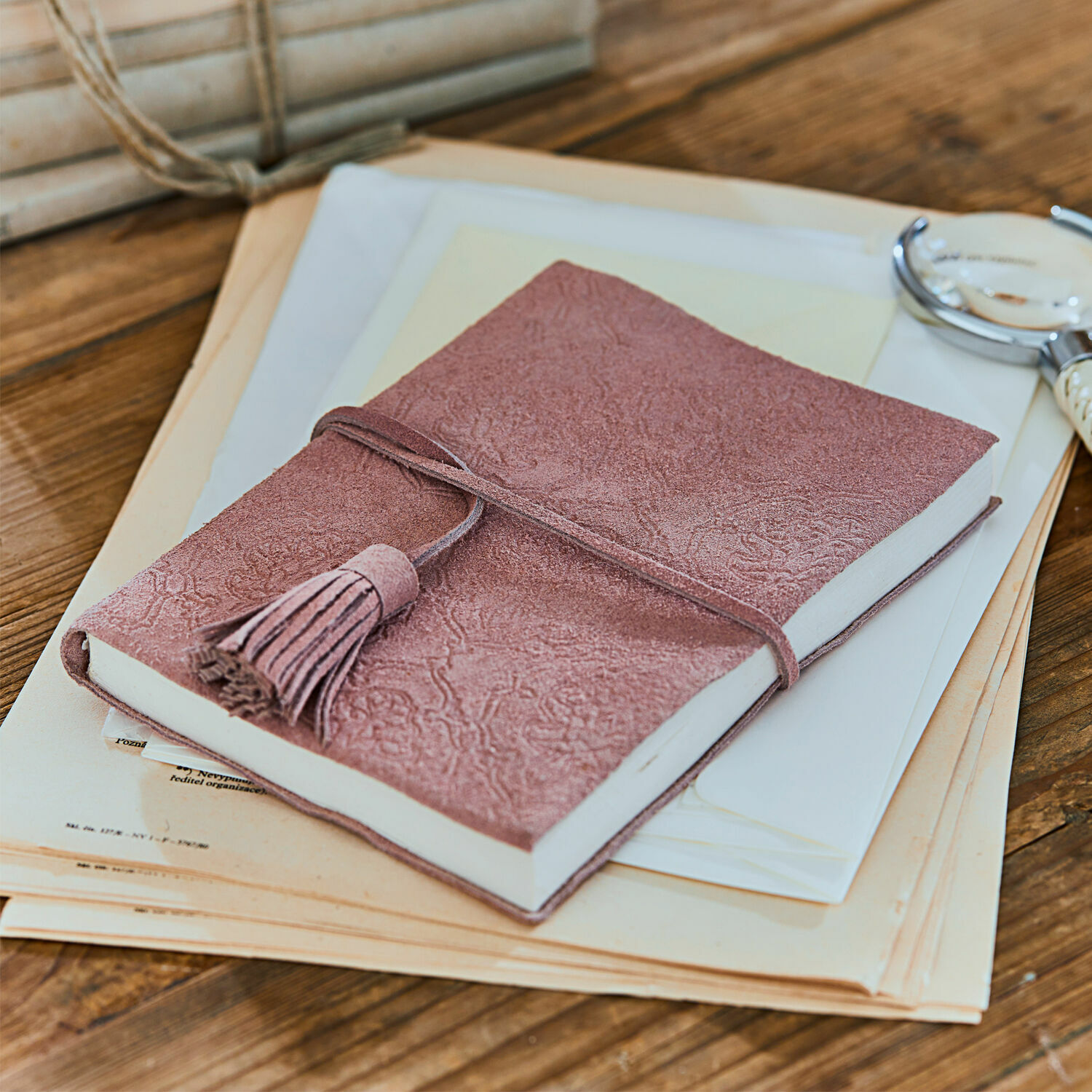 Carnet Orcival Carnet rose en daim avec pompon sur table en bois avec documents, accessoires d'écriture