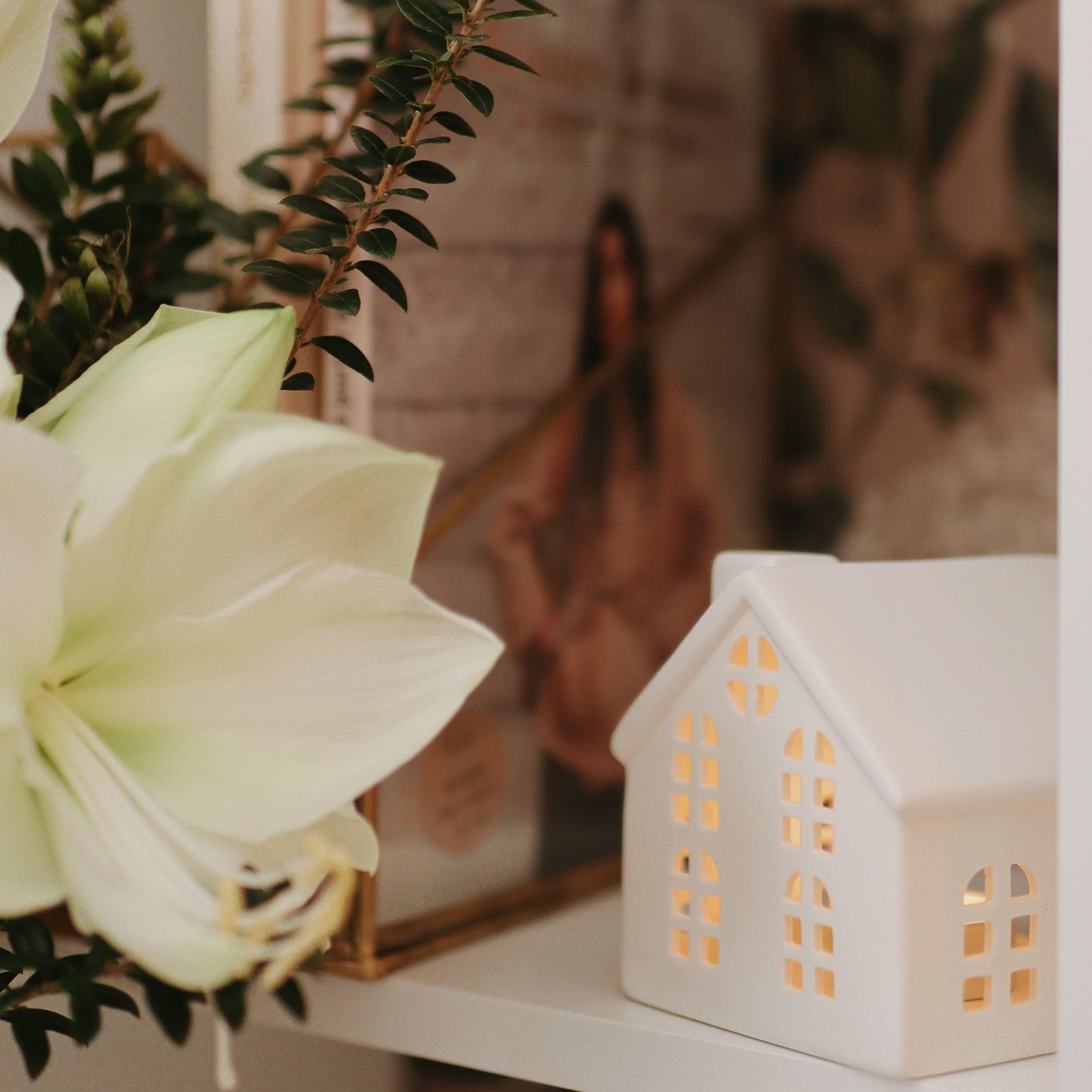 Décoration maison en céramique blanche éclairée sur une étagère avec fleur blanche et feuillage vert