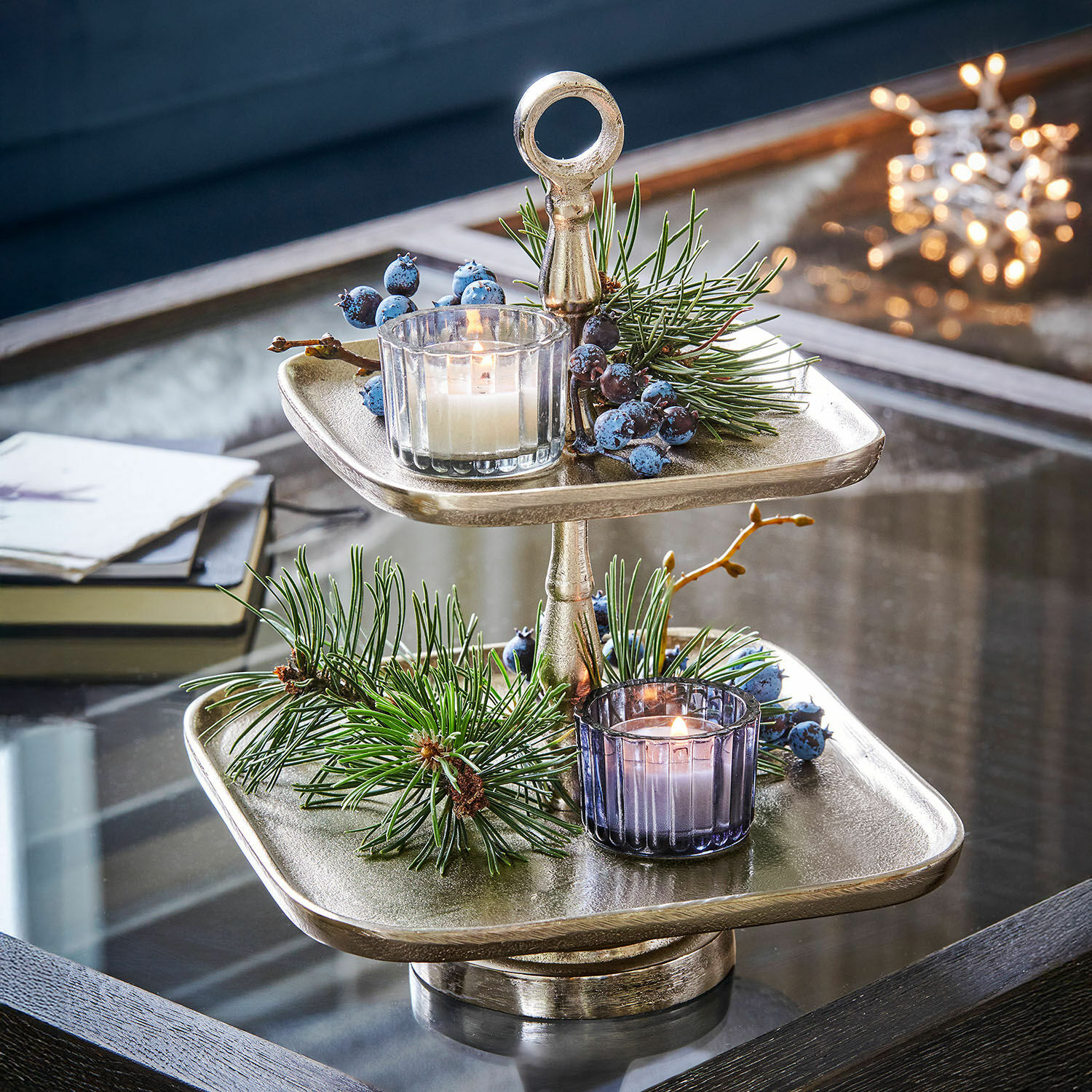 Présentoir à étages Tuarla Présentoir à deux niveaux en métal argenté avec décorations de Noël et bougies sur table en verre