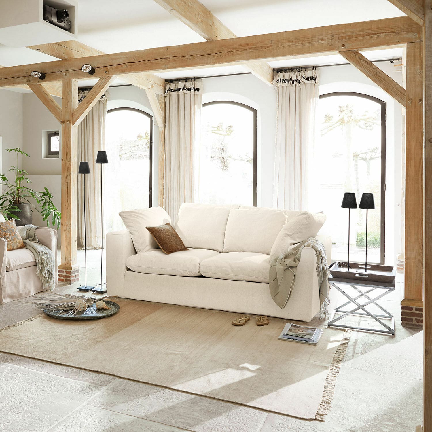 Canapé Xavreille Canapé beige clair en tissu dans un salon lumineux avec poutres en bois et tapis clair