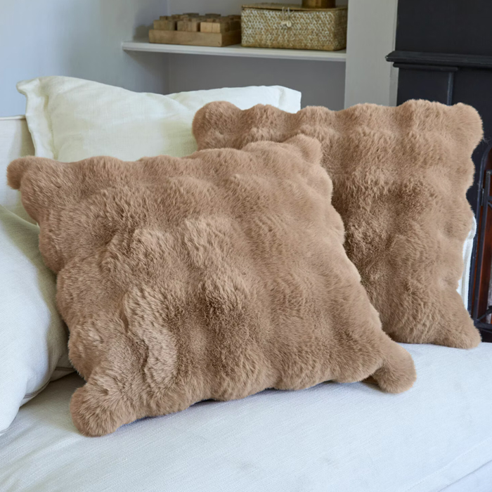 Coussins beige doux en matière pelucheuse sur un canapé clair, décoration intérieure confortable
