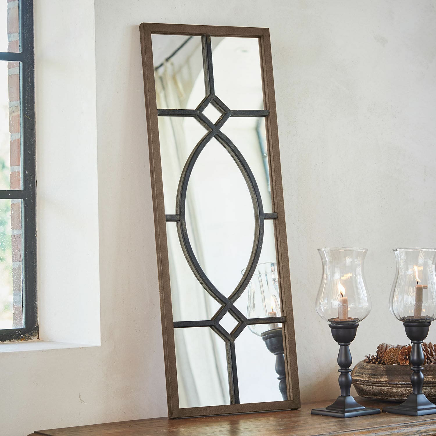 Miroir Millery Miroir rectangulaire avec cadre en bois brun et motif métallique noir posé sur une table avec des lanternes