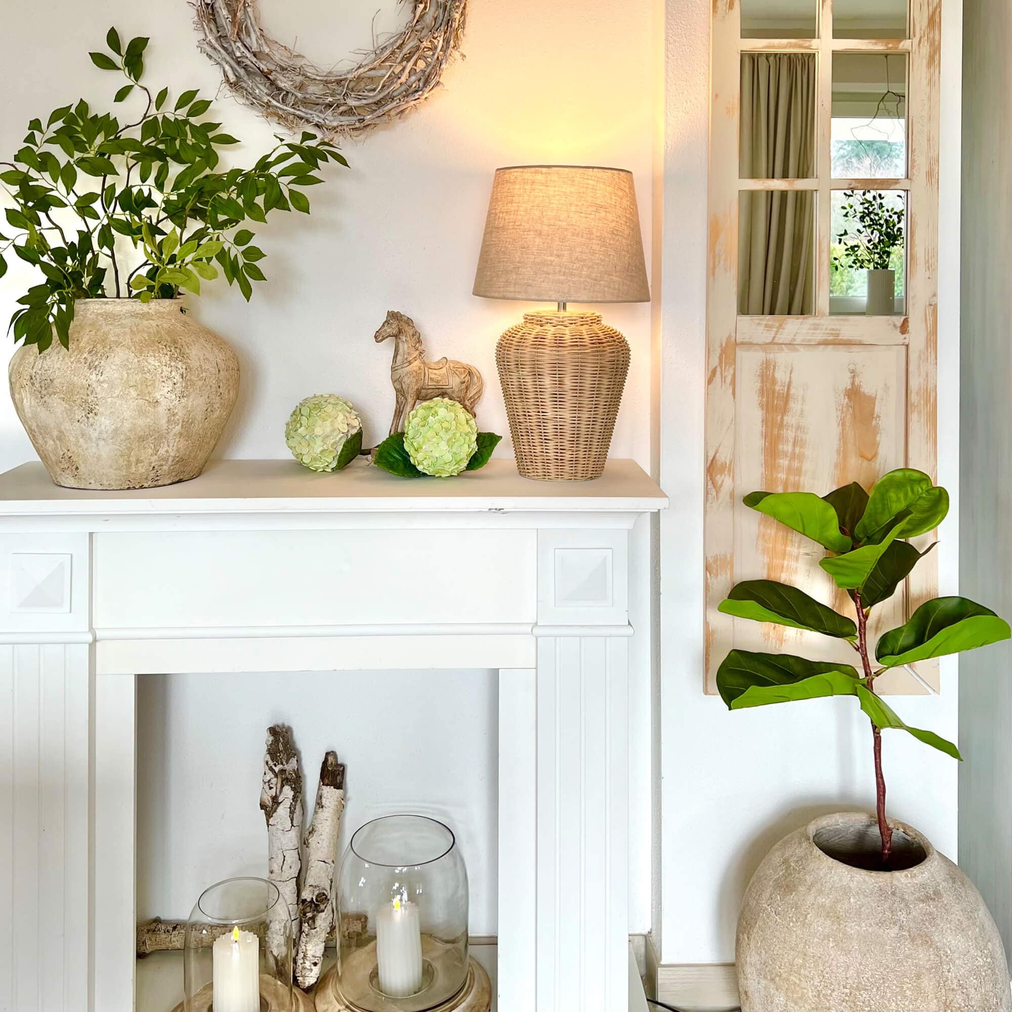 Cheminée blanche décorative avec lampe en rotin et plantes vertes en pots en pierre
