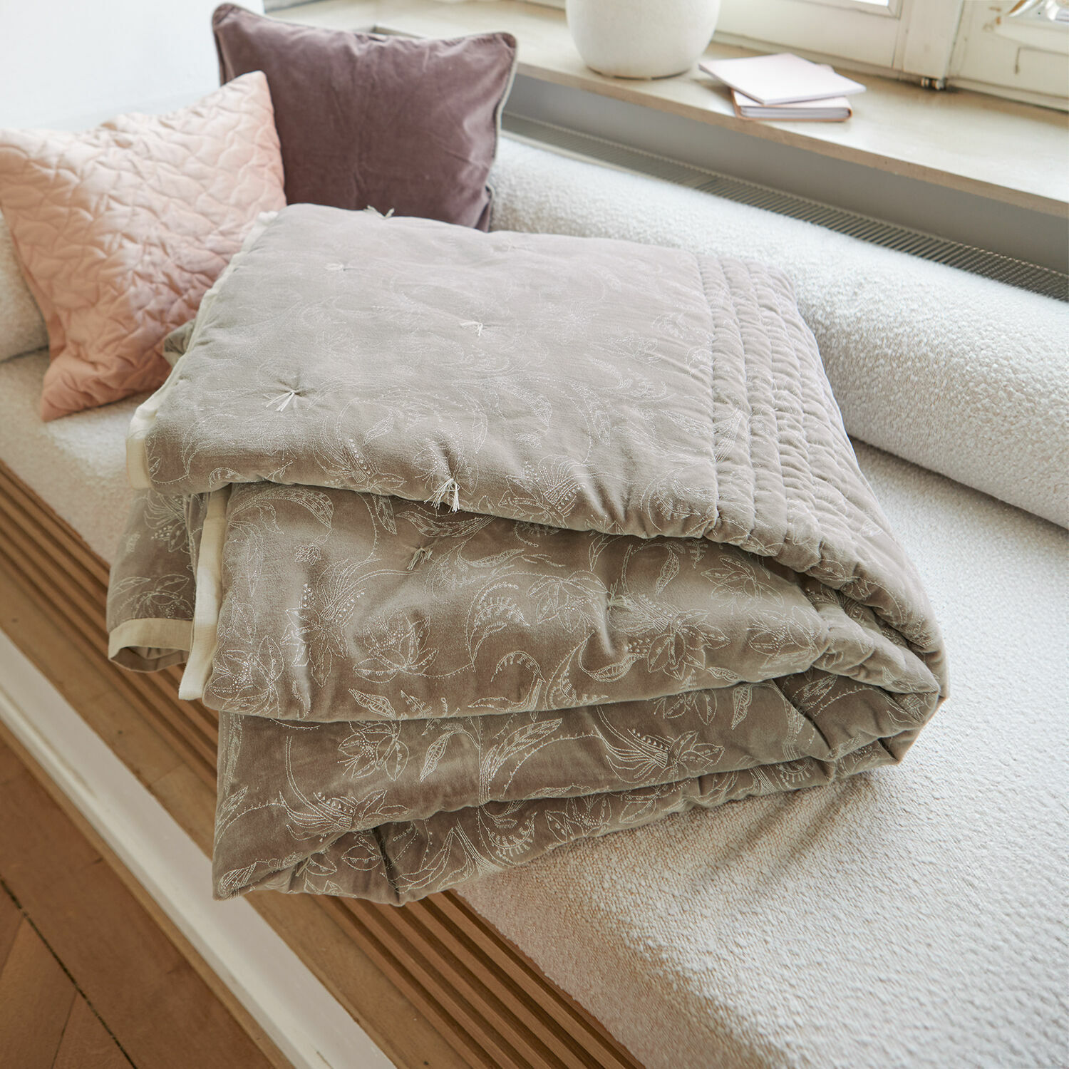 Courtepointe Olicianne Plaid matelassé beige avec motif floral délicat posé sur un canapé clair dans un salon