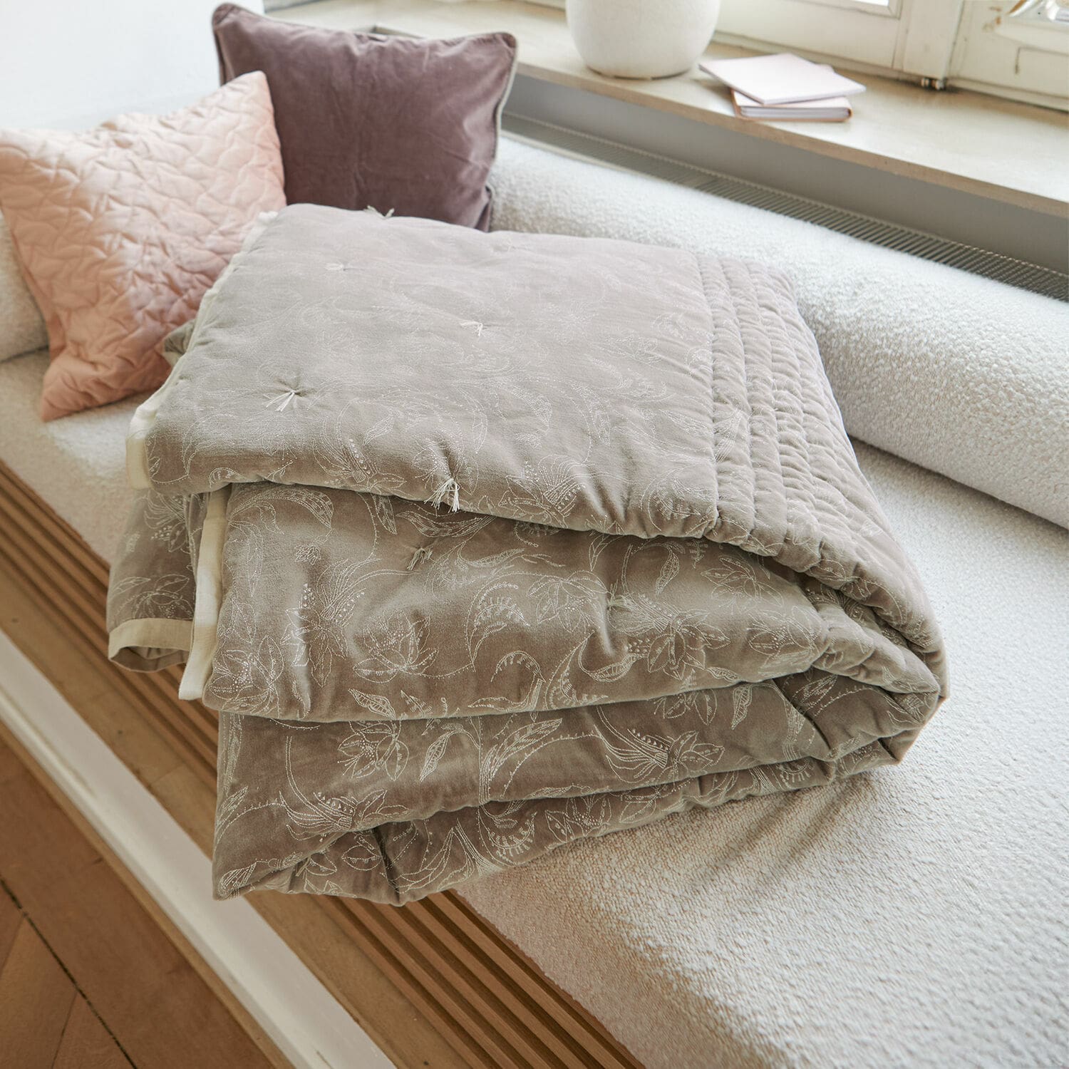 Courtepointe Olicianne Plaid matelassé beige avec motif floral délicat posé sur un canapé clair dans un salon