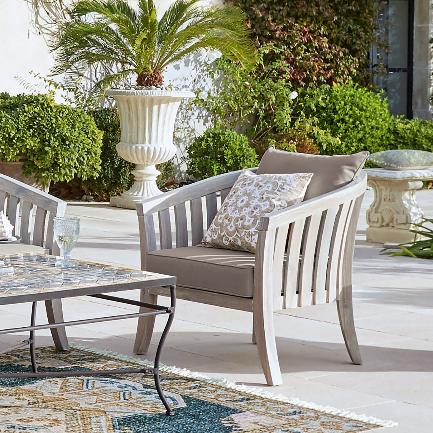 Fauteuil Seanad Fauteuil de jardin en bois clair avec coussins beige sur terrasse entourée de plantes vertes