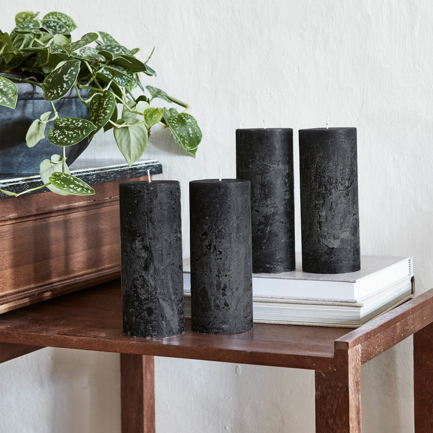 Lot de 4 bougies Homel Quatre bougies noires en cire sur une table en bois à côté d'une plante verte en pot