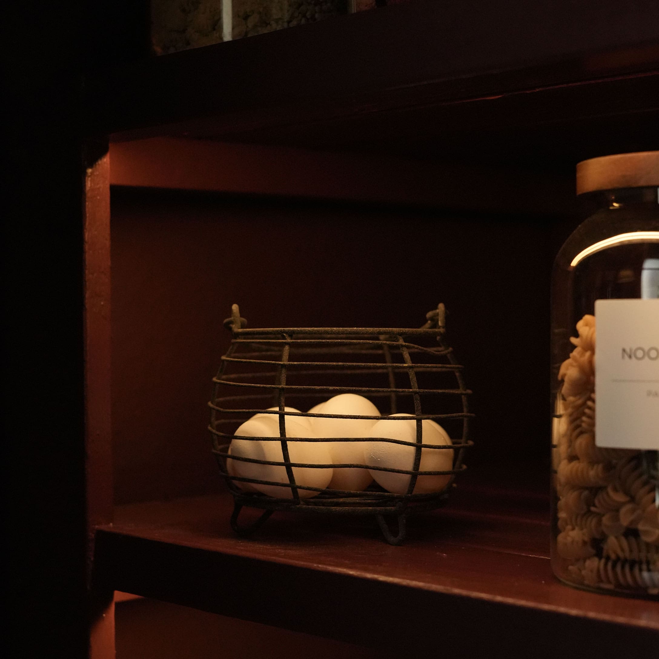 Panier en métal avec des œufs blancs sur une étagère en bois sombre dans un intérieur rustique