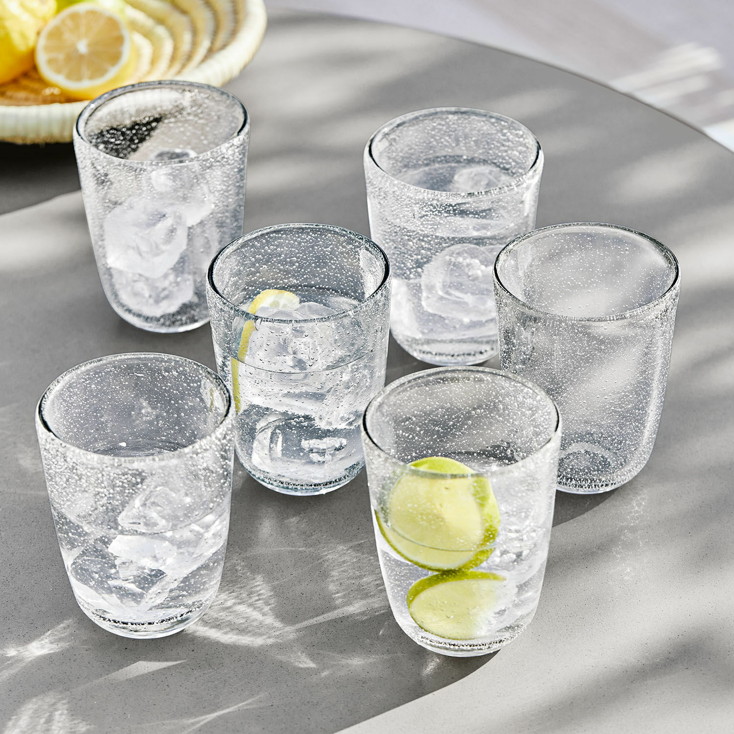 Ensemble de six verres en verre transparent à bulles avec glaçons et tranches de citron sur table grise