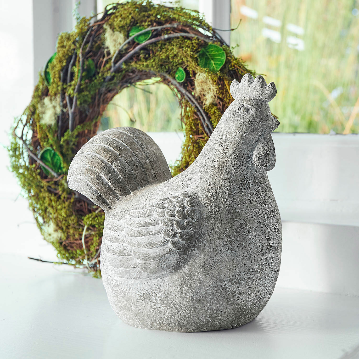 Poule décorative Roselique Figurine décorative de poule grise en béton sur fond clair avec une couronne verte en arrière-plan