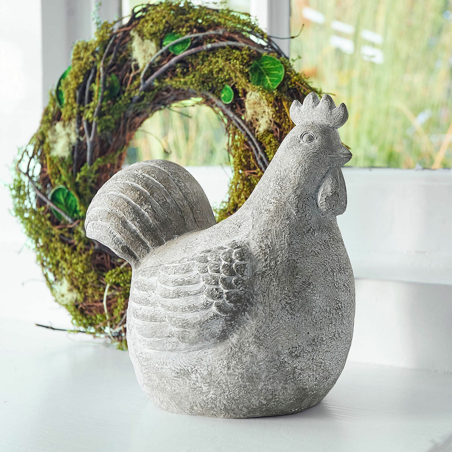 Poule décorative Roselique Figurine décorative de poule grise en béton sur fond clair avec une couronne verte en arrière-plan