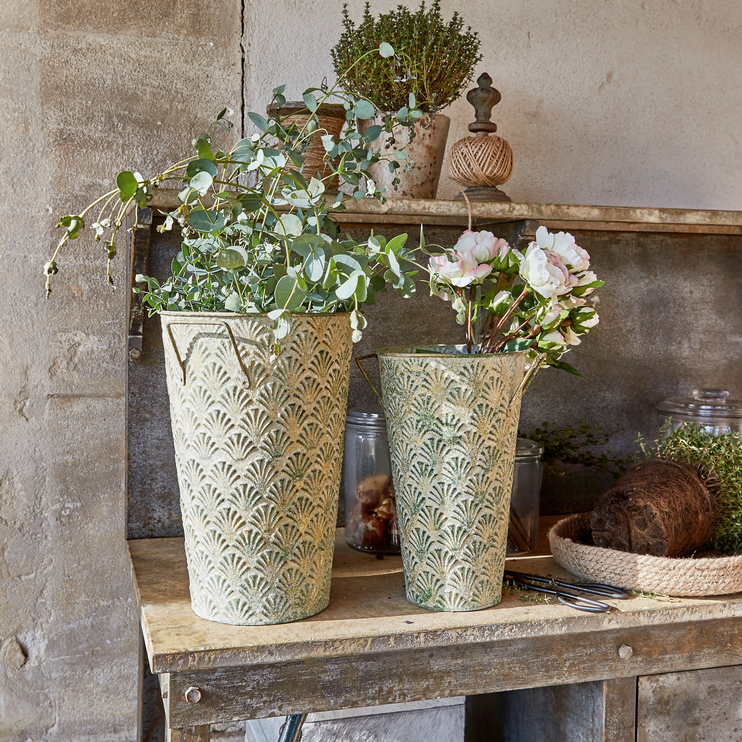 Lot de 2 vases décoratifs Iskele Deux pots décoratifs en métal vert-beige avec plantes sur une table rustique en bois