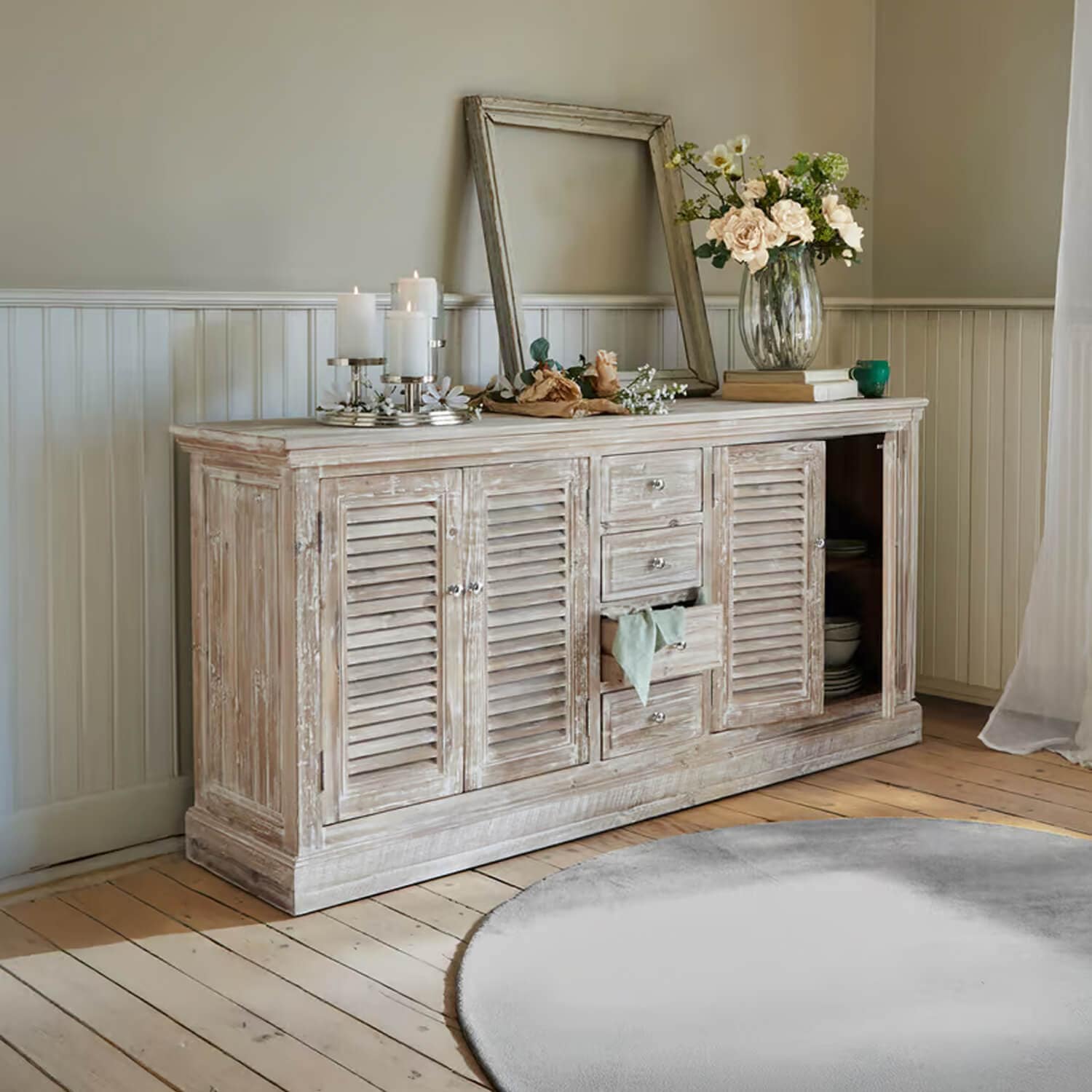 Buffet rustique en bois blanc patiné avec décorations et bougies dans un salon lumineux