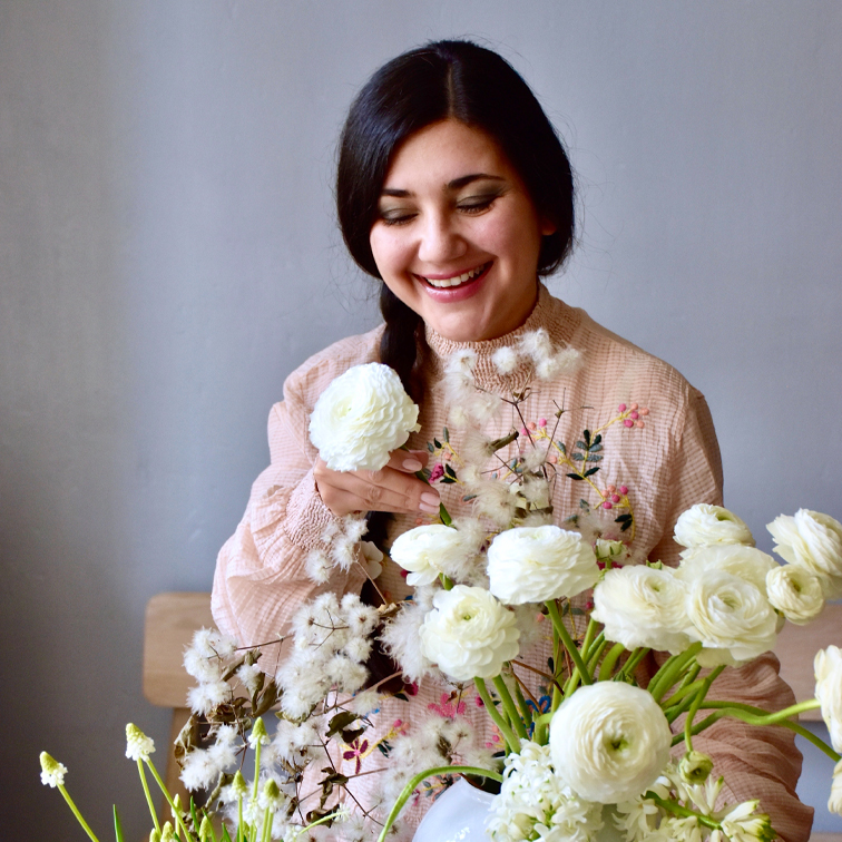 Femme souriante en blouse pastel arrangeant des fleurs blanches dans un vase, décoration printanière