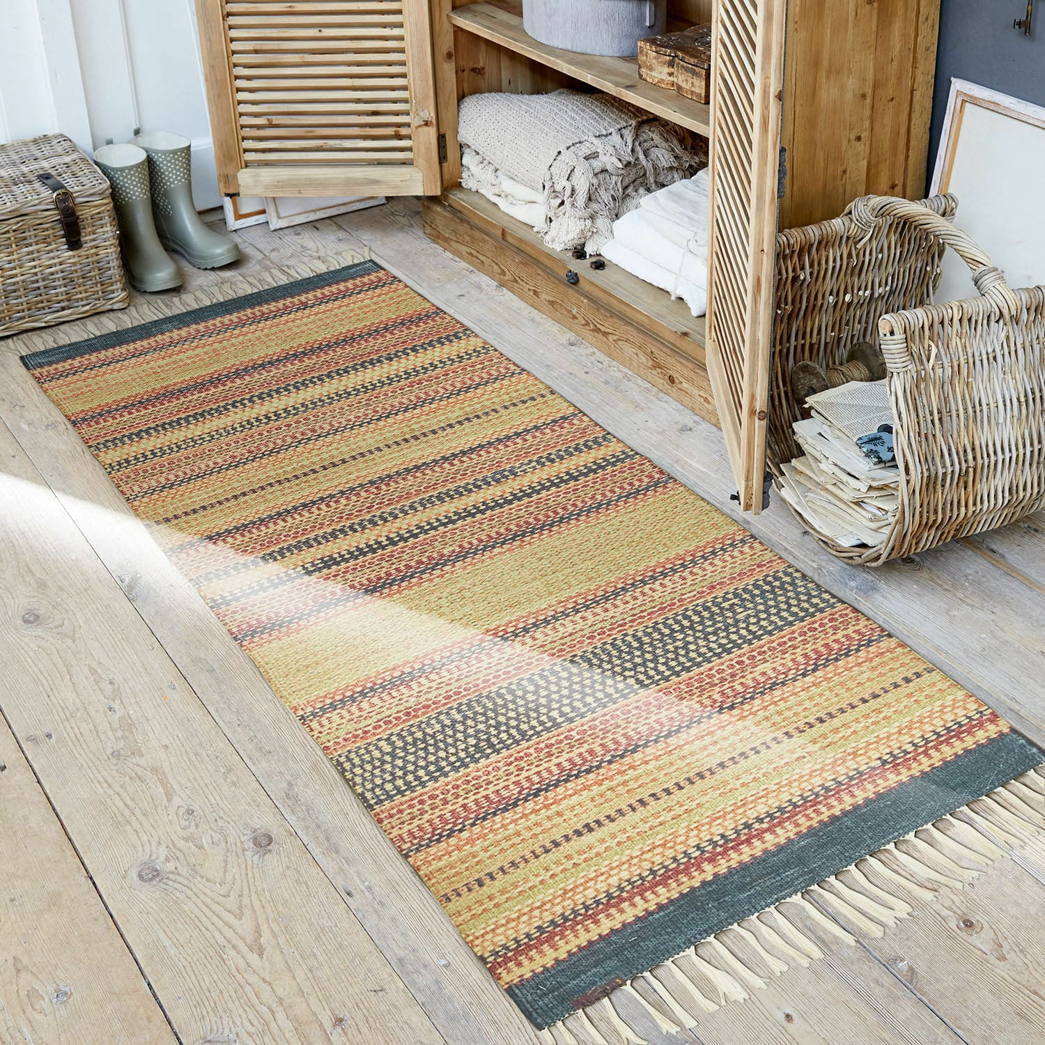 Tapis d’extérieur et d’intérieur Atlanta Tapis rayé aux tons chauds avec franges sur un sol en bois dans un intérieur rustique