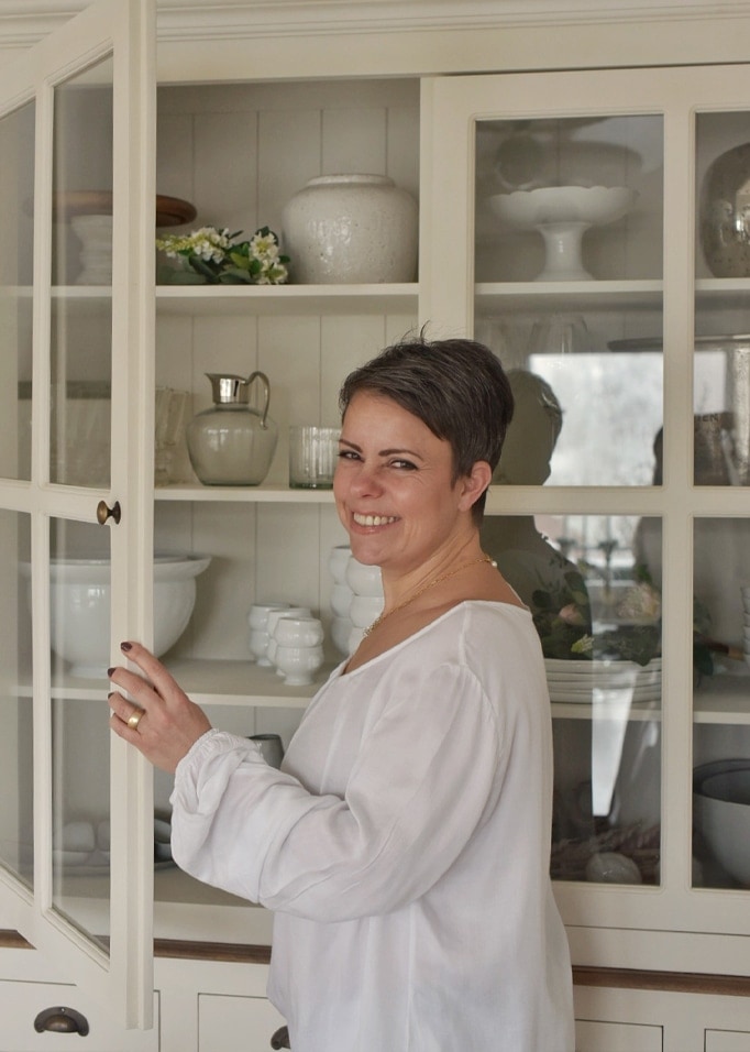Femme en blouse blanche ouvrant un buffet crème avec vaisselle en porcelaine et décorations