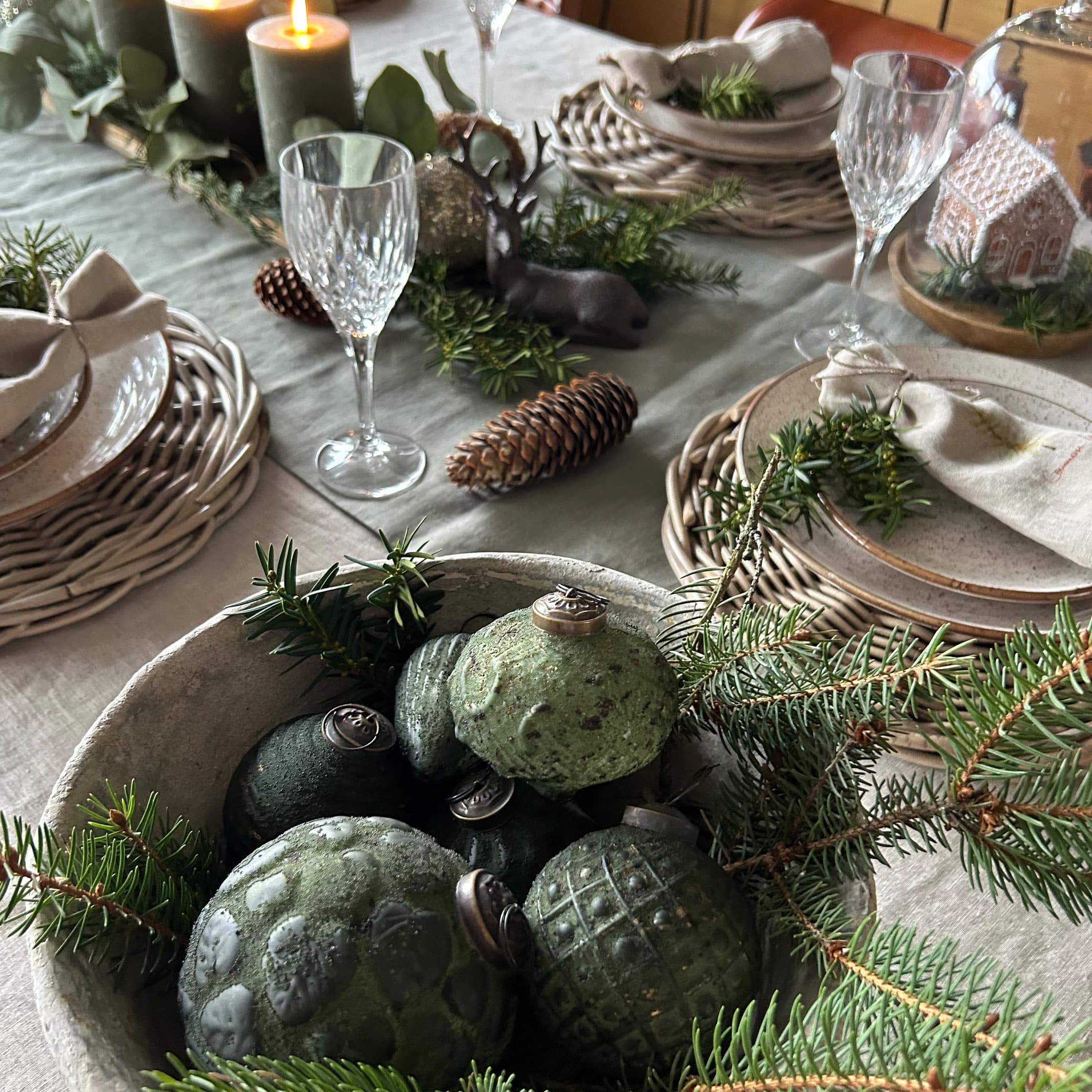 Boules de Noël vertes en céramique dans un bol avec branches de sapin sur une table décorée