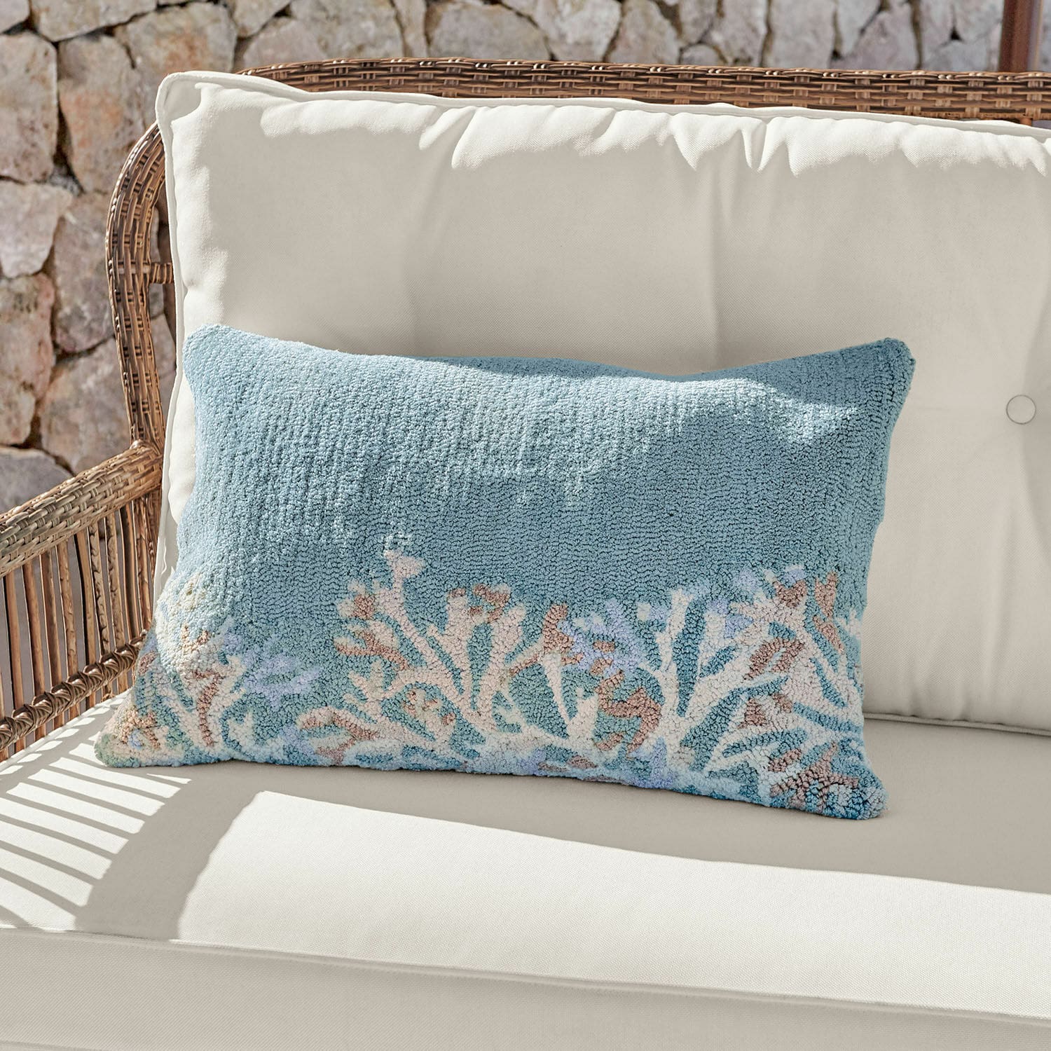 Housse de coussin d'intérieur et d'extérieur Dorlancourt Coussin décoratif bleu en tissu doux avec motif corail posé sur un canapé en rotin clair.