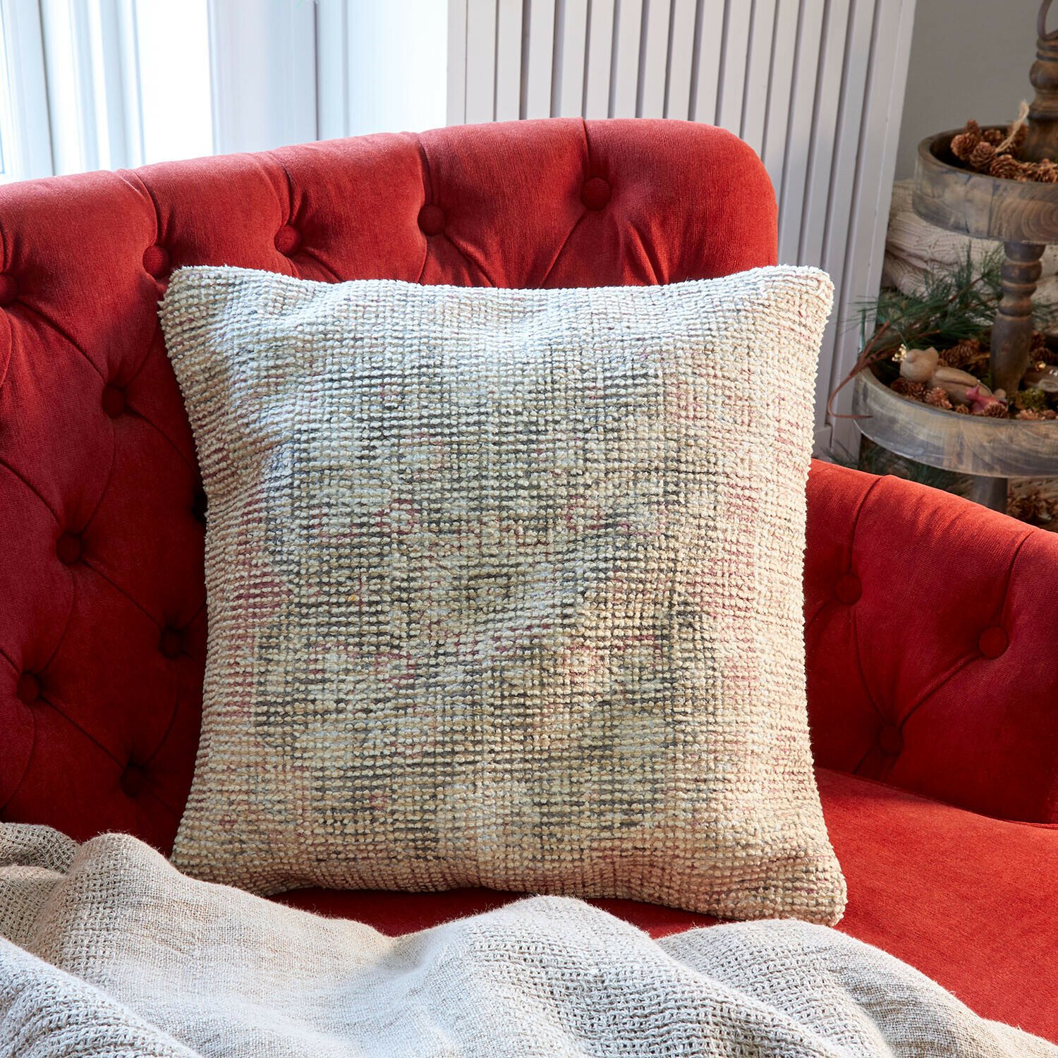 Housse de coussin Kaelun Coussin décoratif beige en tissu doux sur un canapé rouge capitonné dans un salon lumineux