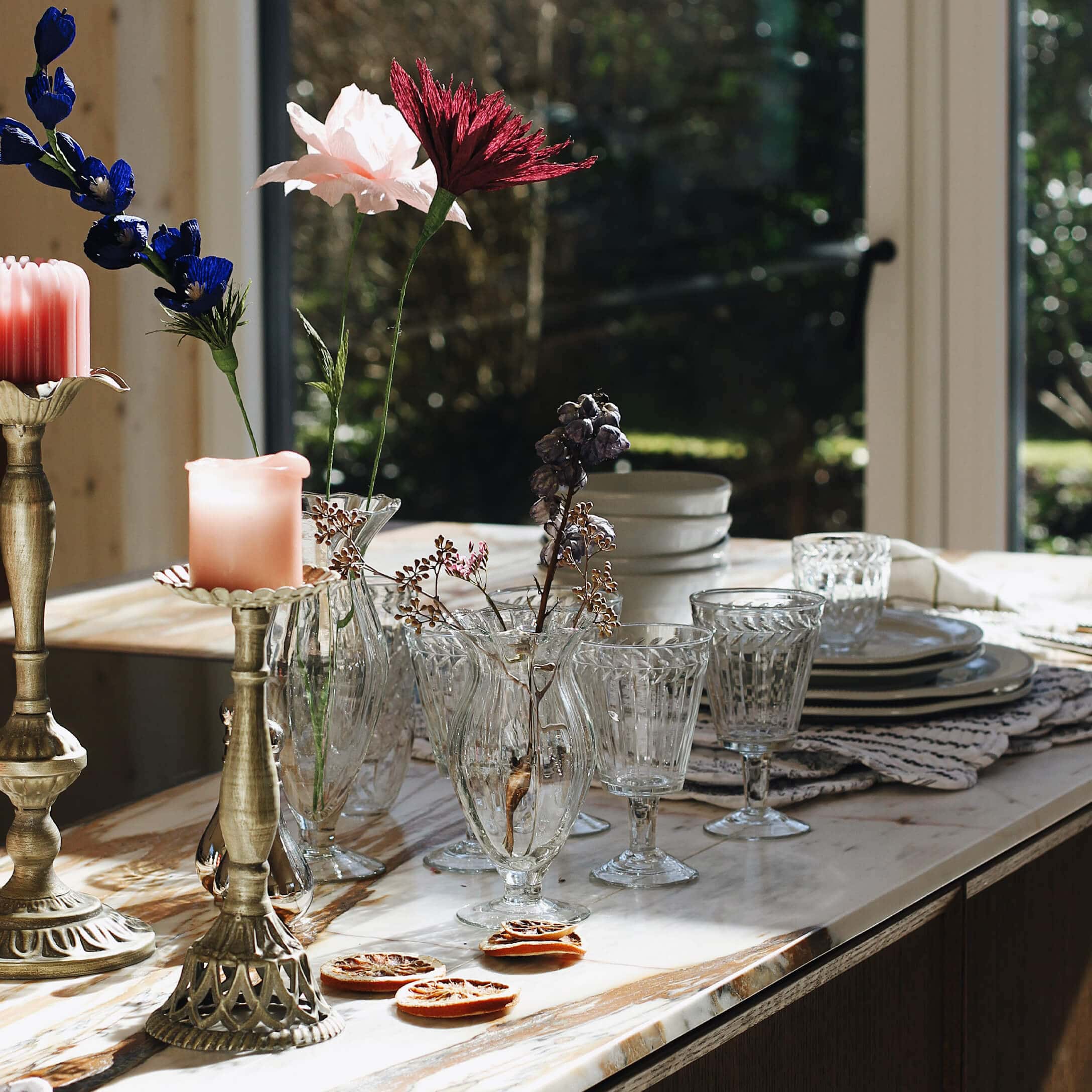 Vases et verres en verre sur un plan de travail en marbre avec fleurs séchées et bougies décoratives