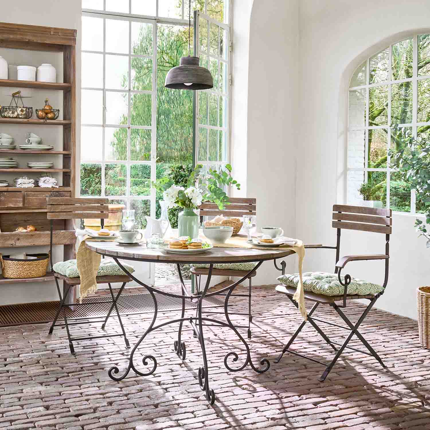 Table ronde en bois avec pieds en métal et chaises avec coussins dans une salle à manger lumineuse et ensoleillée