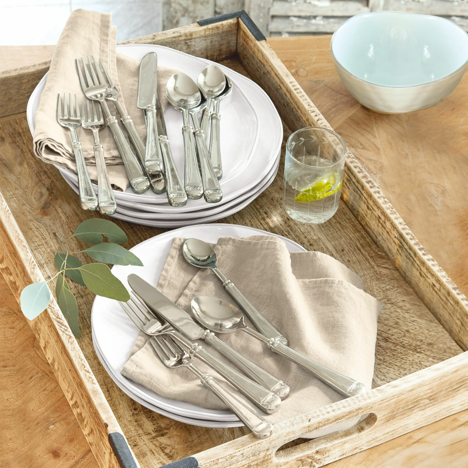 Couverts Eriat Ensemble de couverts argentés sur assiettes blanches avec serviettes beiges sur plateau en bois
