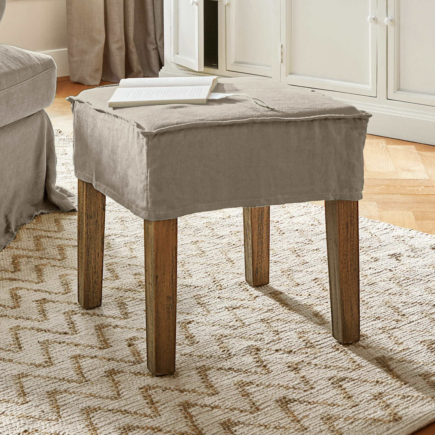 Tabouret Vionnique Pouf beige avec housse en coton et pieds en bois sur tapis clair dans un salon lumineux