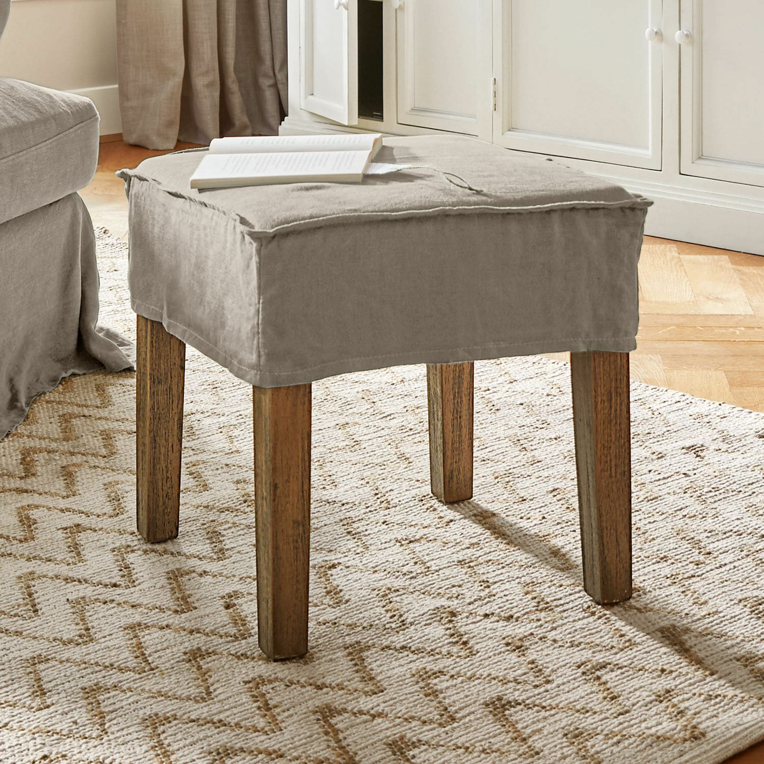Tabouret Vionnique Pouf beige avec housse en coton et pieds en bois sur tapis clair dans un salon lumineux