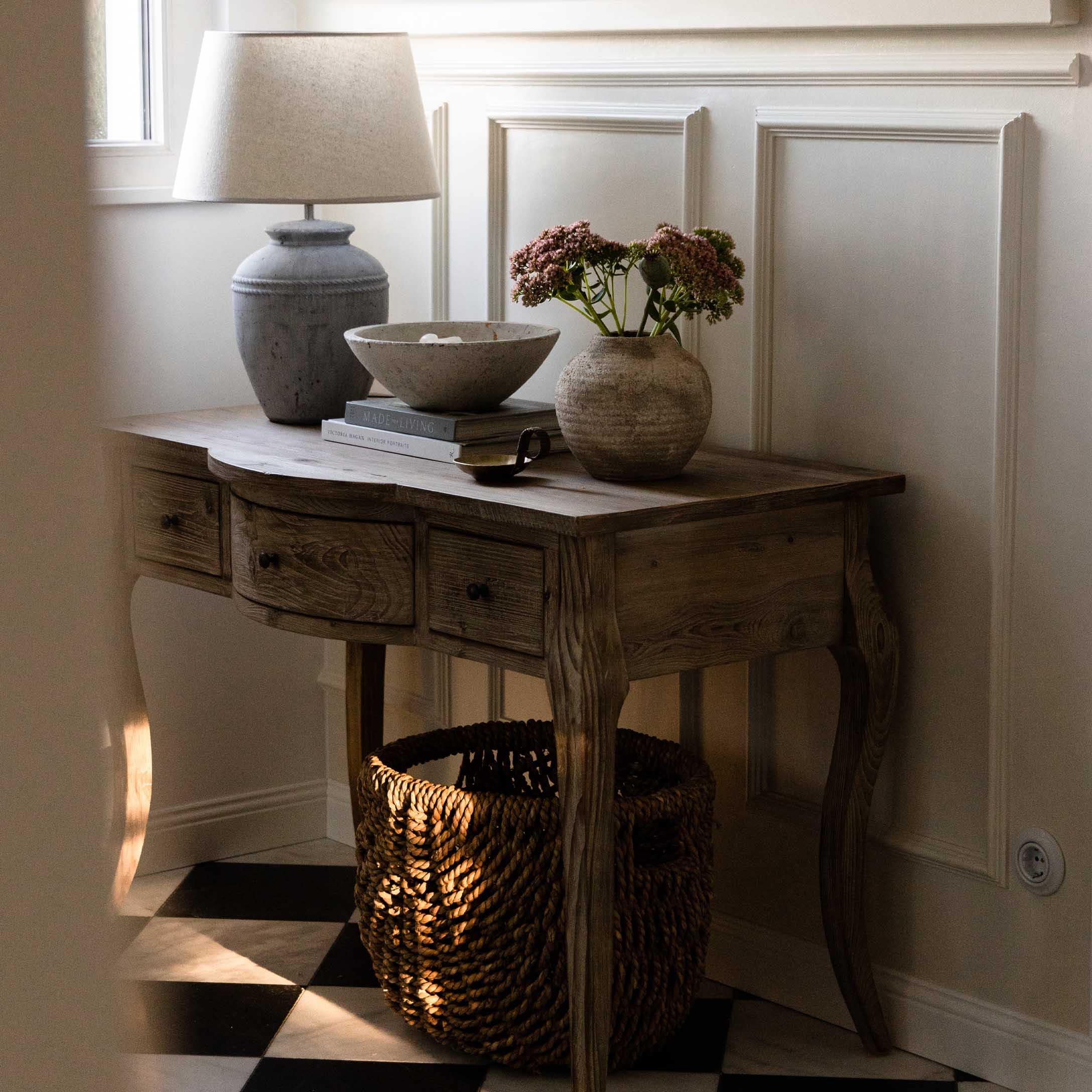 Table en bois avec tiroirs, lampe, vase et panier sur sol en damier noir et blanc