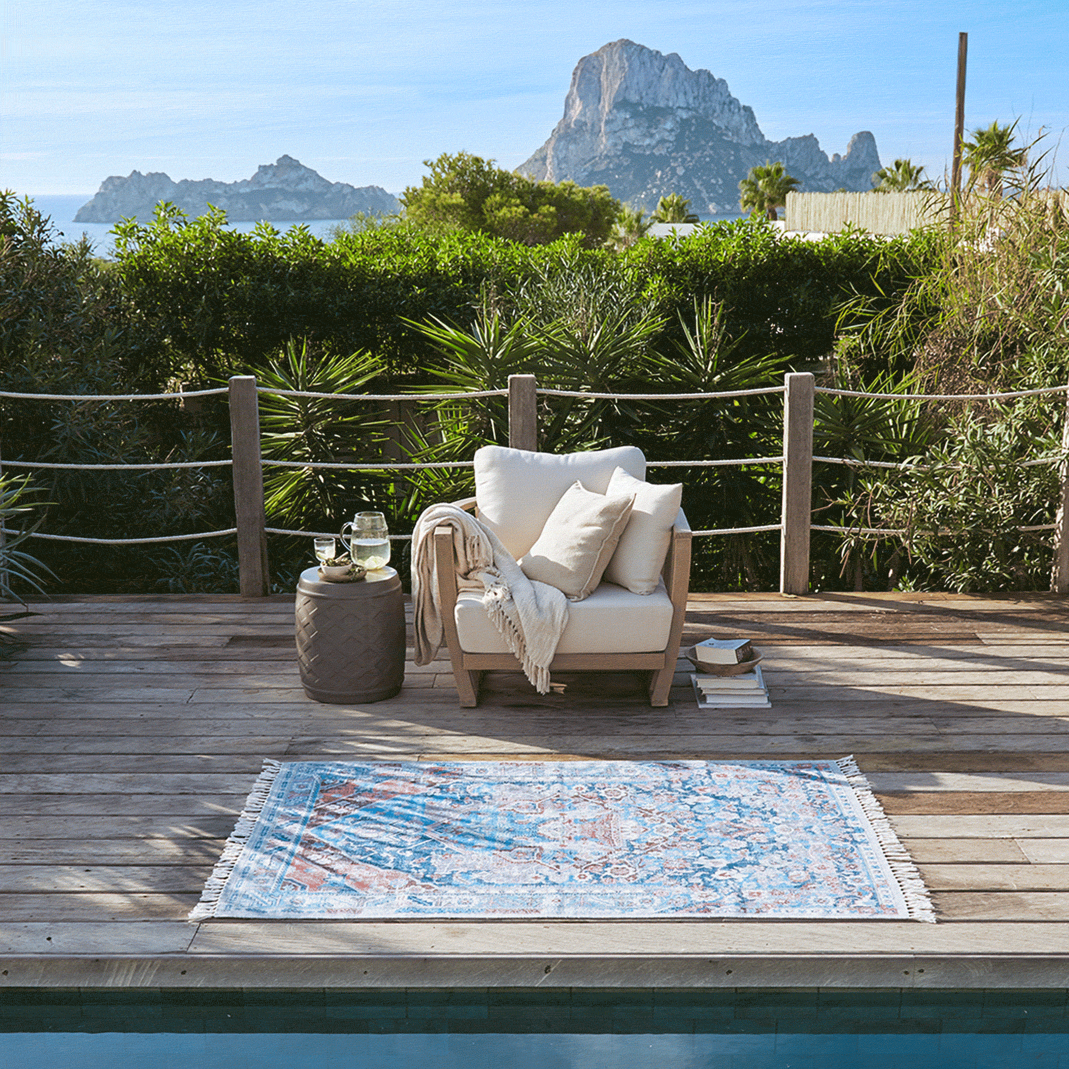Terrasse en bois avec fauteuil blanc et tapis coloré près de la piscine avec vue sur la montagne