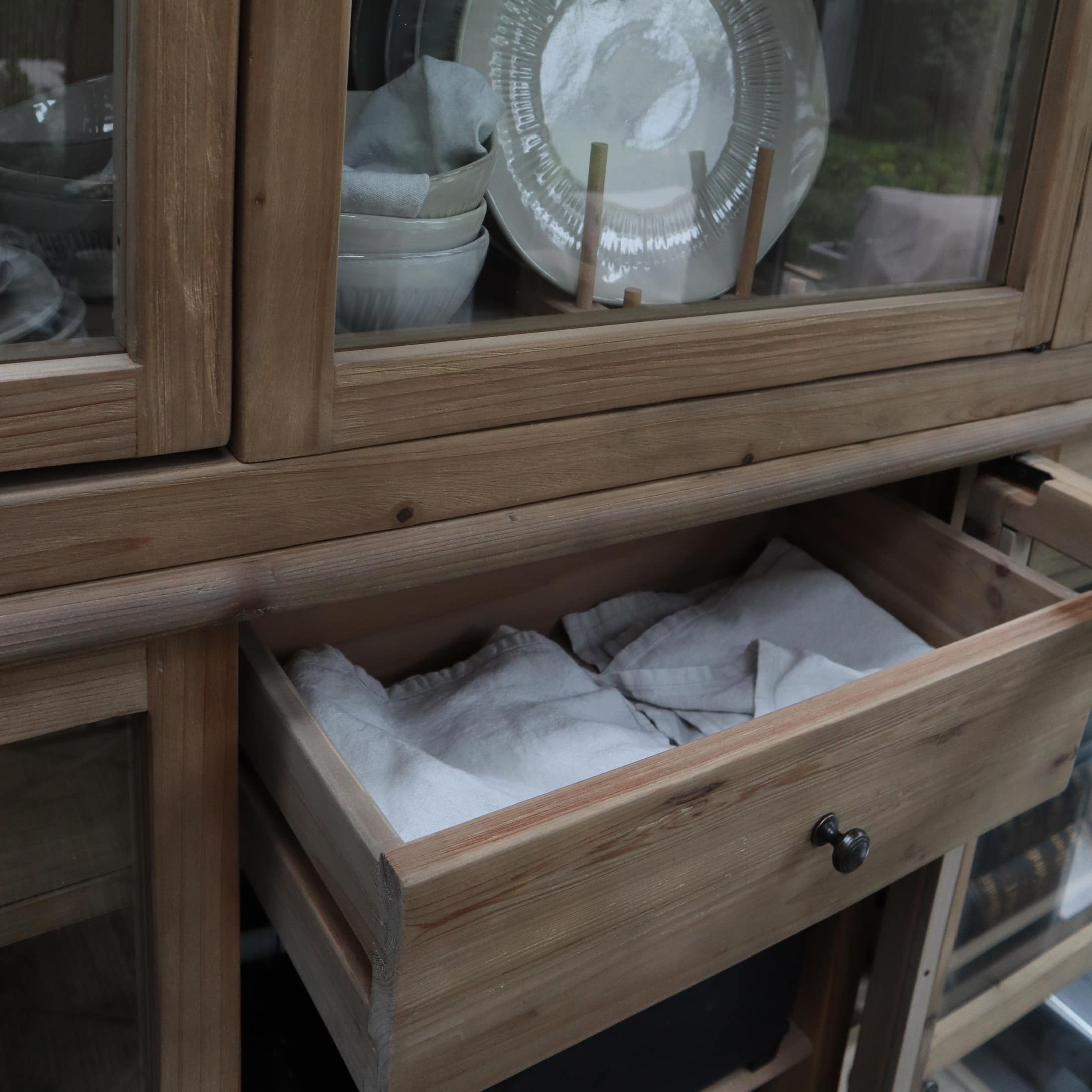 Tiroir en bois clair avec tissu blanc dans une vitrine en bois avec assiettes en céramique