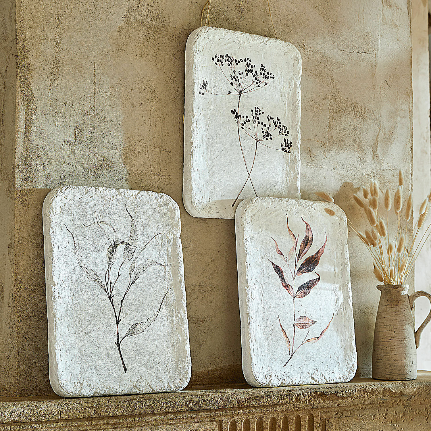 Lot de 3 tableaux Hillsdale Trois décorations murales blanches avec motifs végétaux sur un mur beige, style naturel et rustique.
