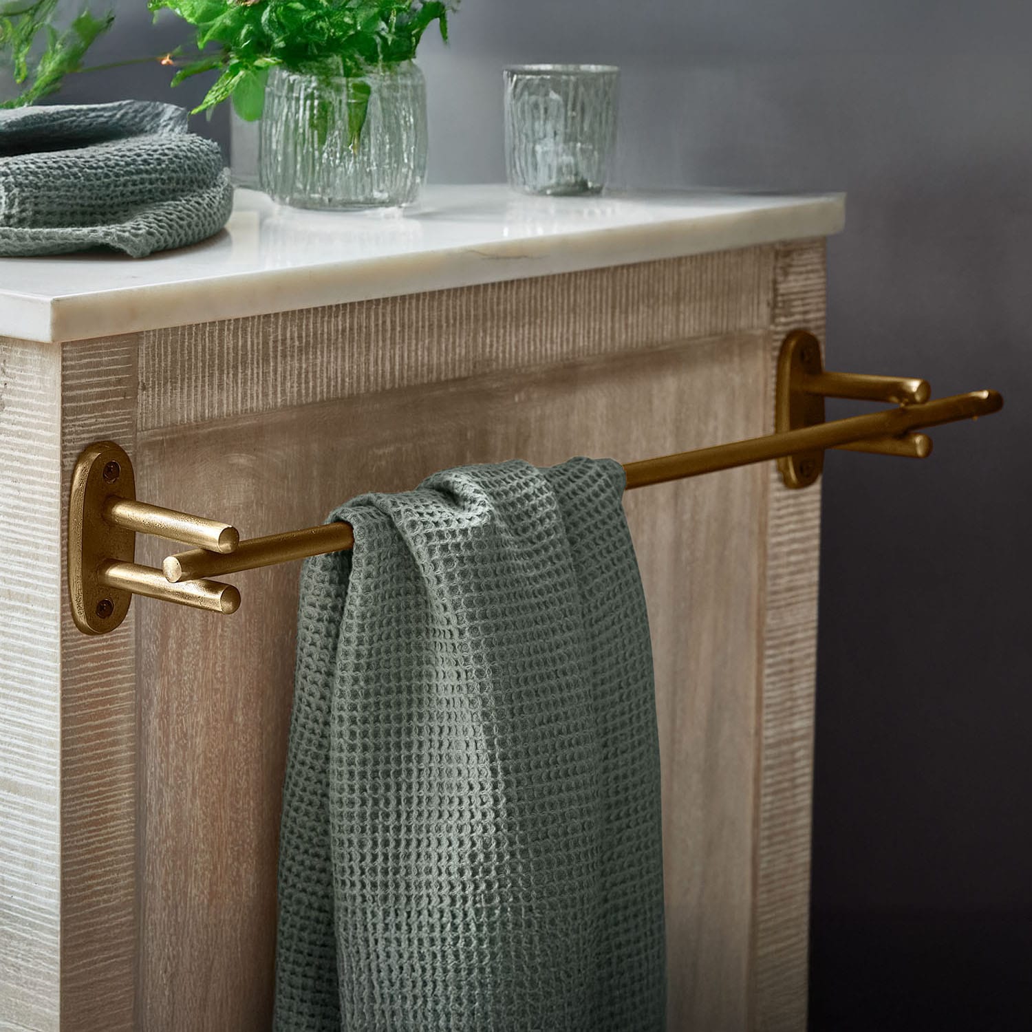 Porte-serviettes en métal doré avec serviette gaufrée verte sur meuble en bois avec plateau en marbre