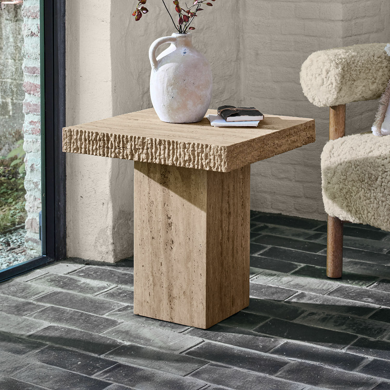 Table d’appoint Gainsbury Table d'appoint carrée en travertin beige posée sur un sol en briques foncées
