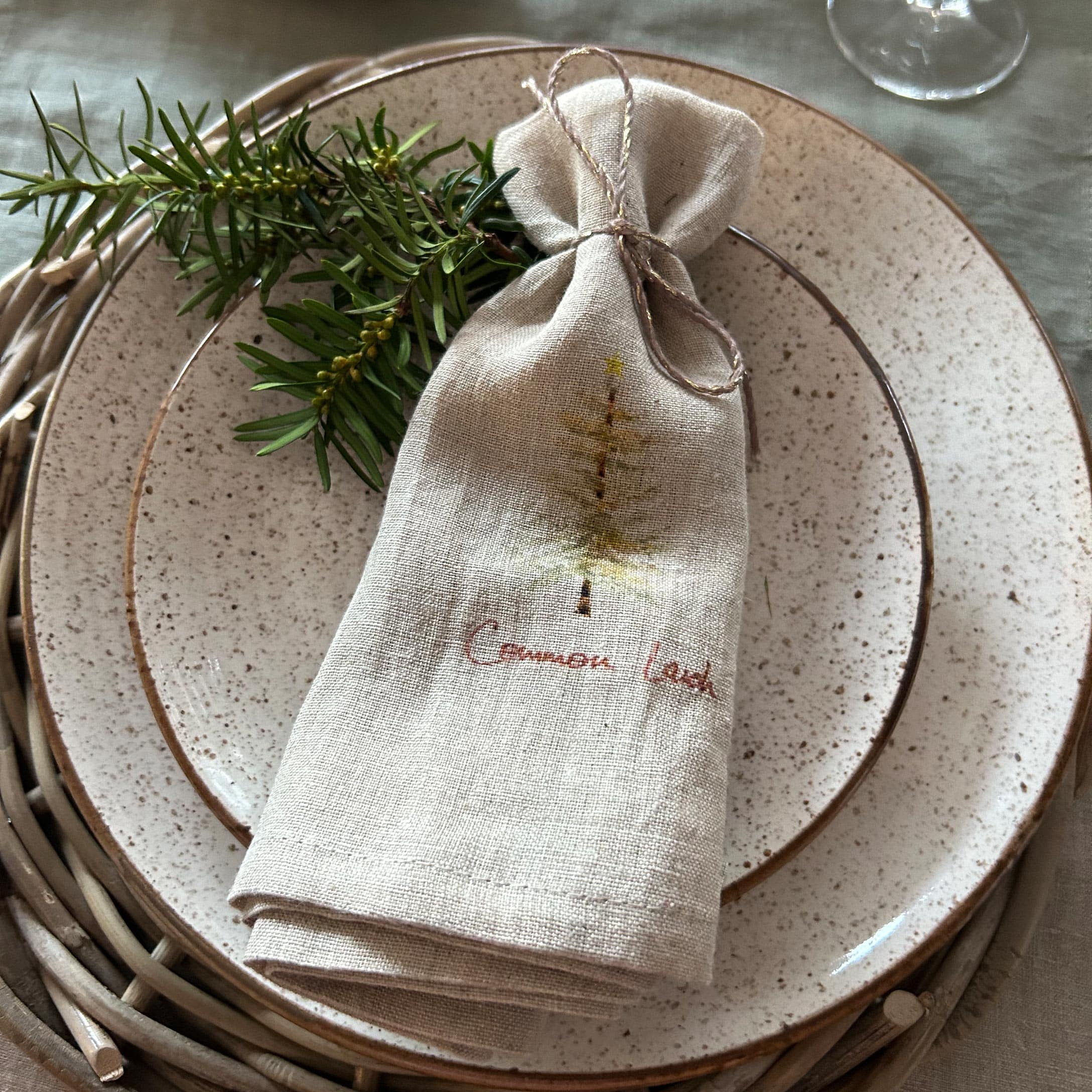Petit sac en lin beige avec motif sapin sur assiette en céramique avec branches vertes