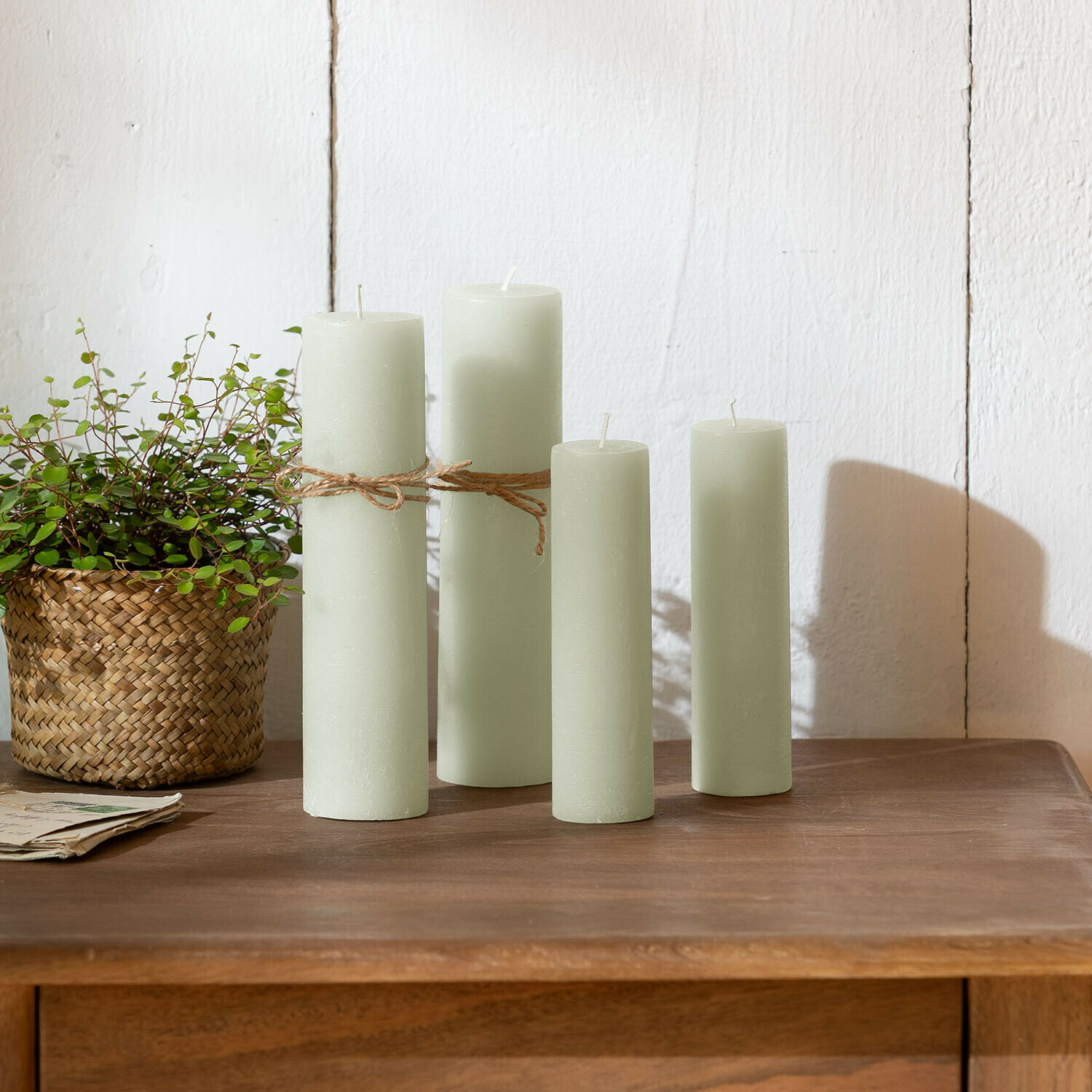 Lot de 4 bougies Avinal Ensemble de quatre bougies vert clair en cire sur une table en bois avec plante en panier tressé