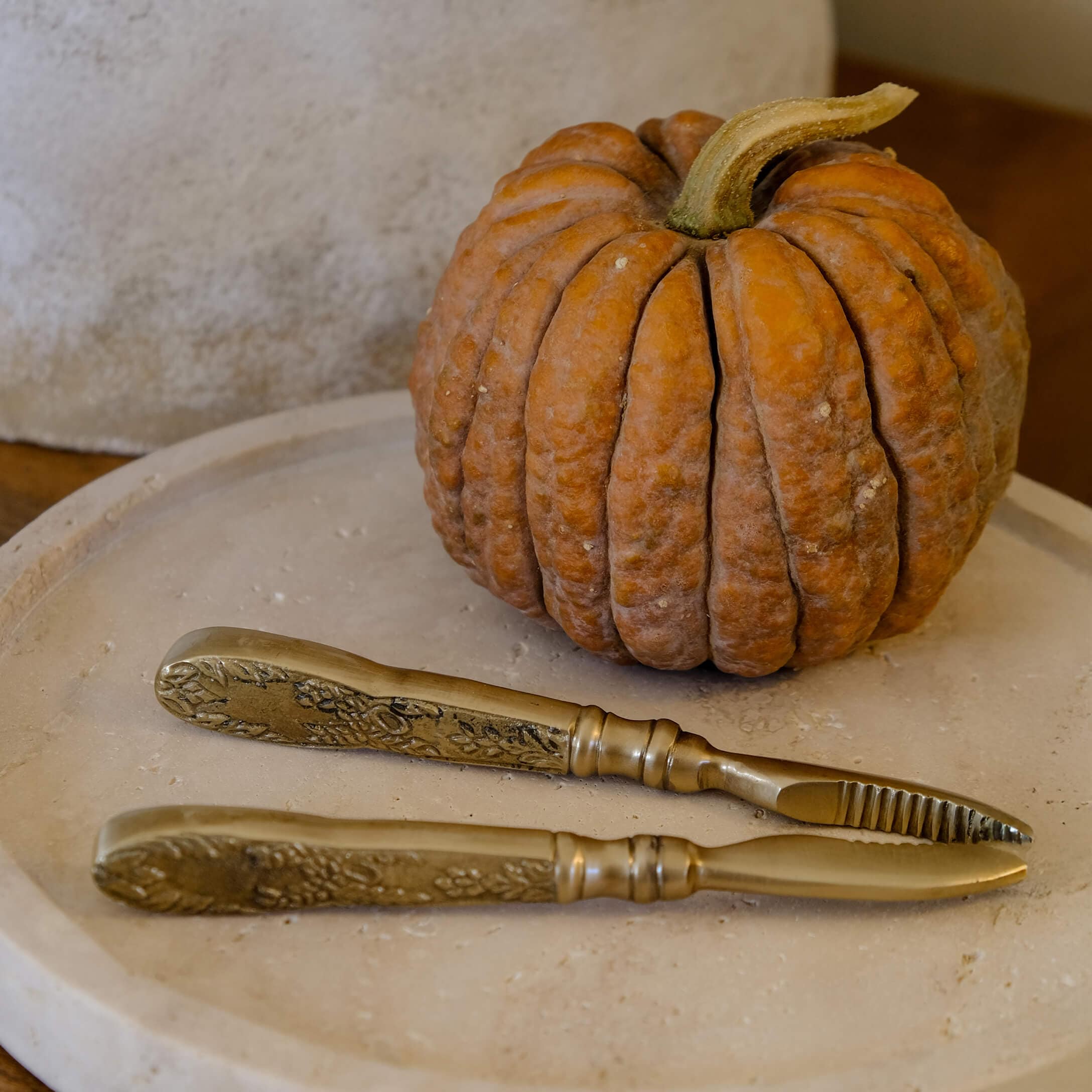 Ensemble de couteaux en laiton avec manches décorés posé sur un plateau beige à côté d'une citrouille orange